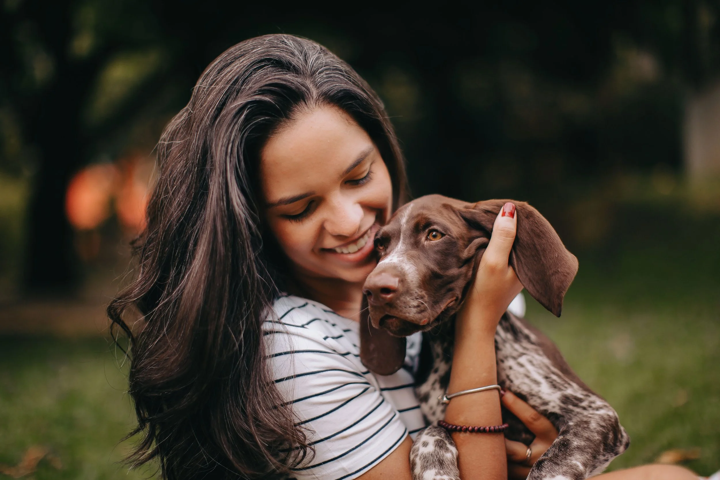 A woman gently holds a young brown and white dog outdoors.