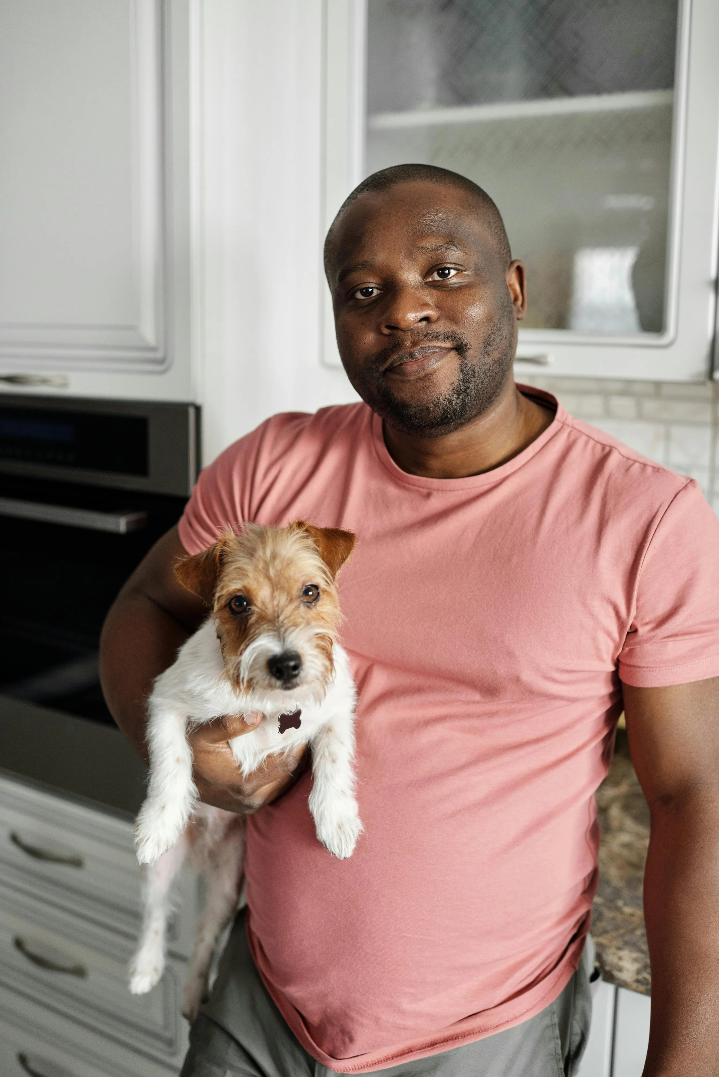 A pet parent holds a small terrier in a bright home kitchen.