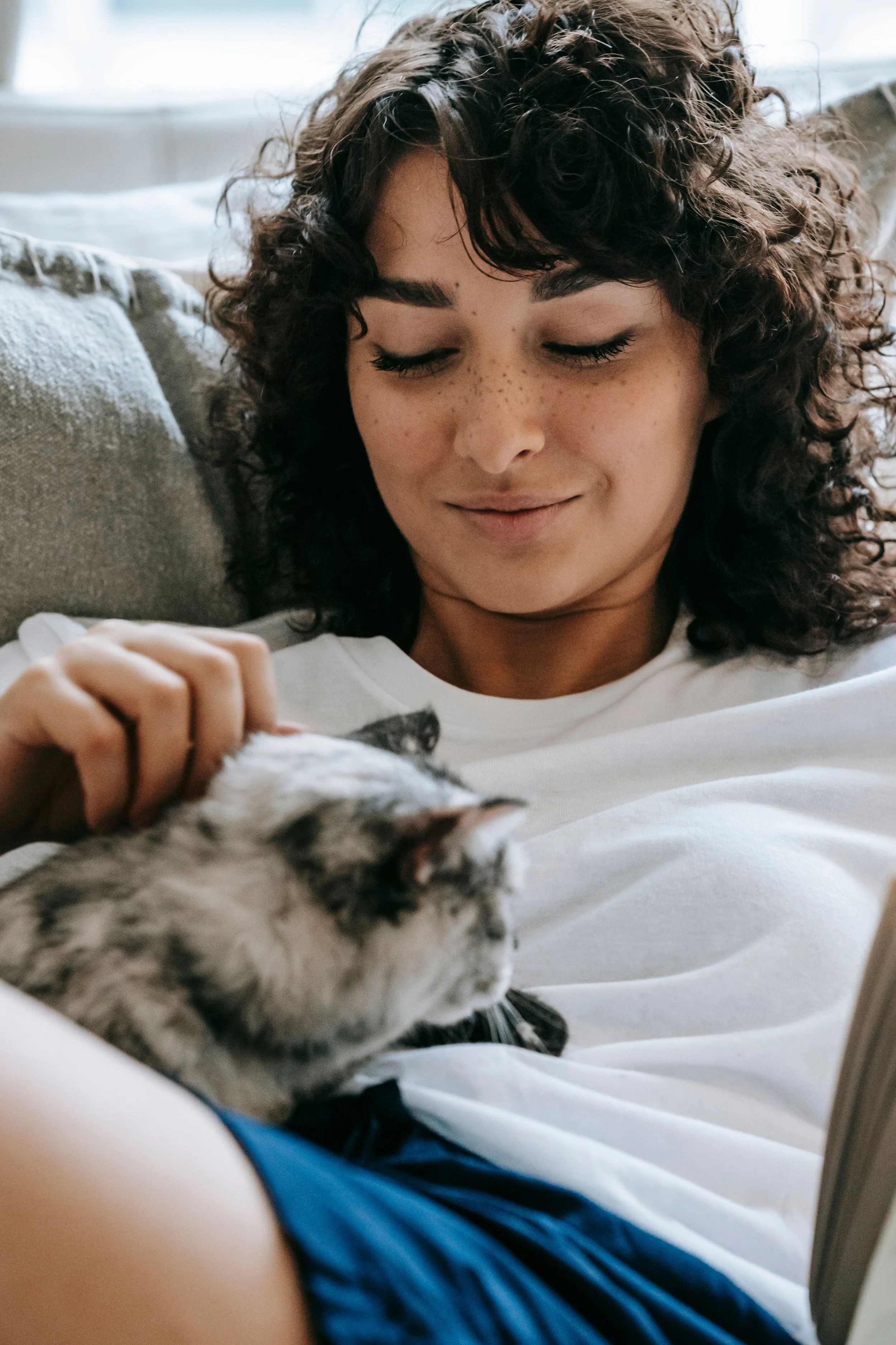 A person rests with a Siamese cat curled against them at home.