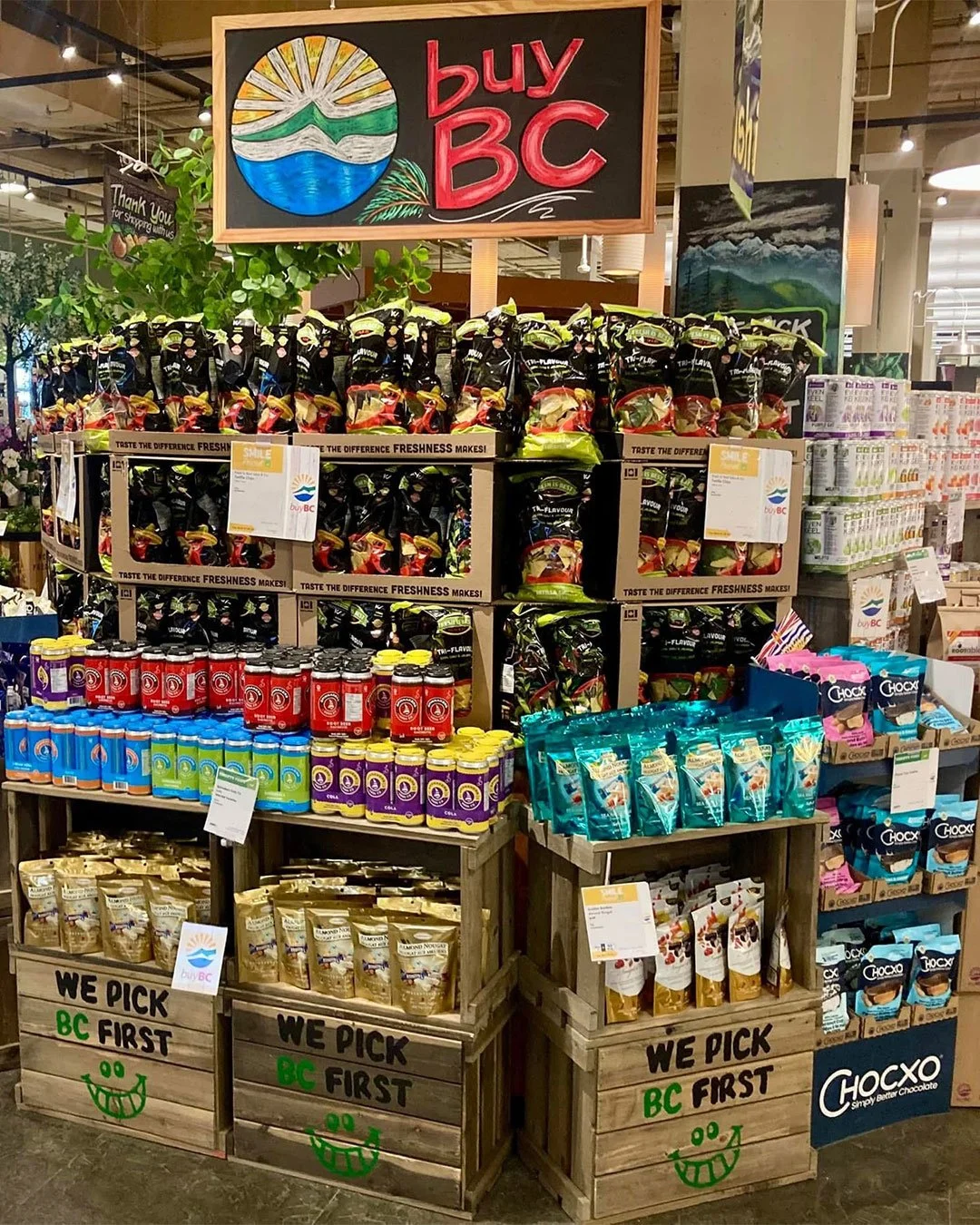 Various BC products on display at a grocery store, including different snacks, sauces, and chocolates, with a sign that says 'buy BC' and a message 'We pick BC first' with a smiling face.