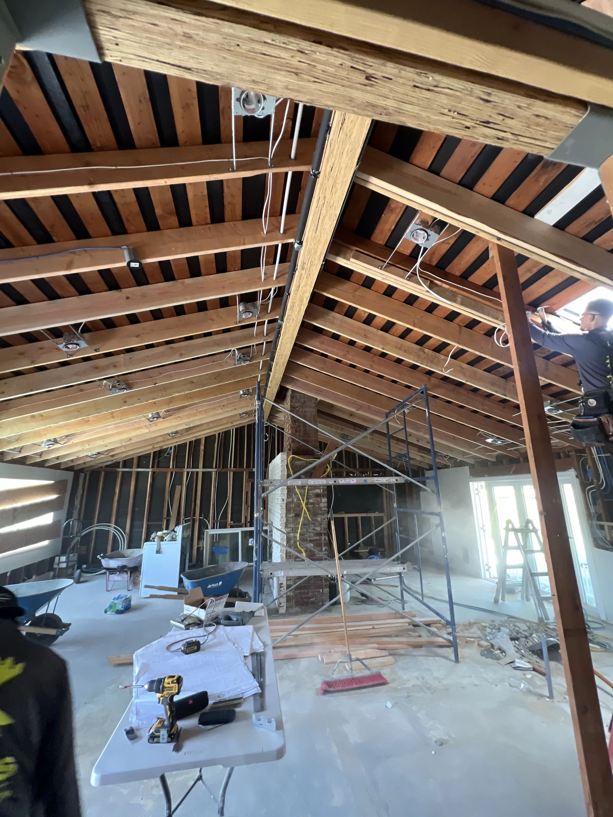 Construction workers installing or working on a wooden ceiling in an unfinished room, with construction tools and equipment scattered around.