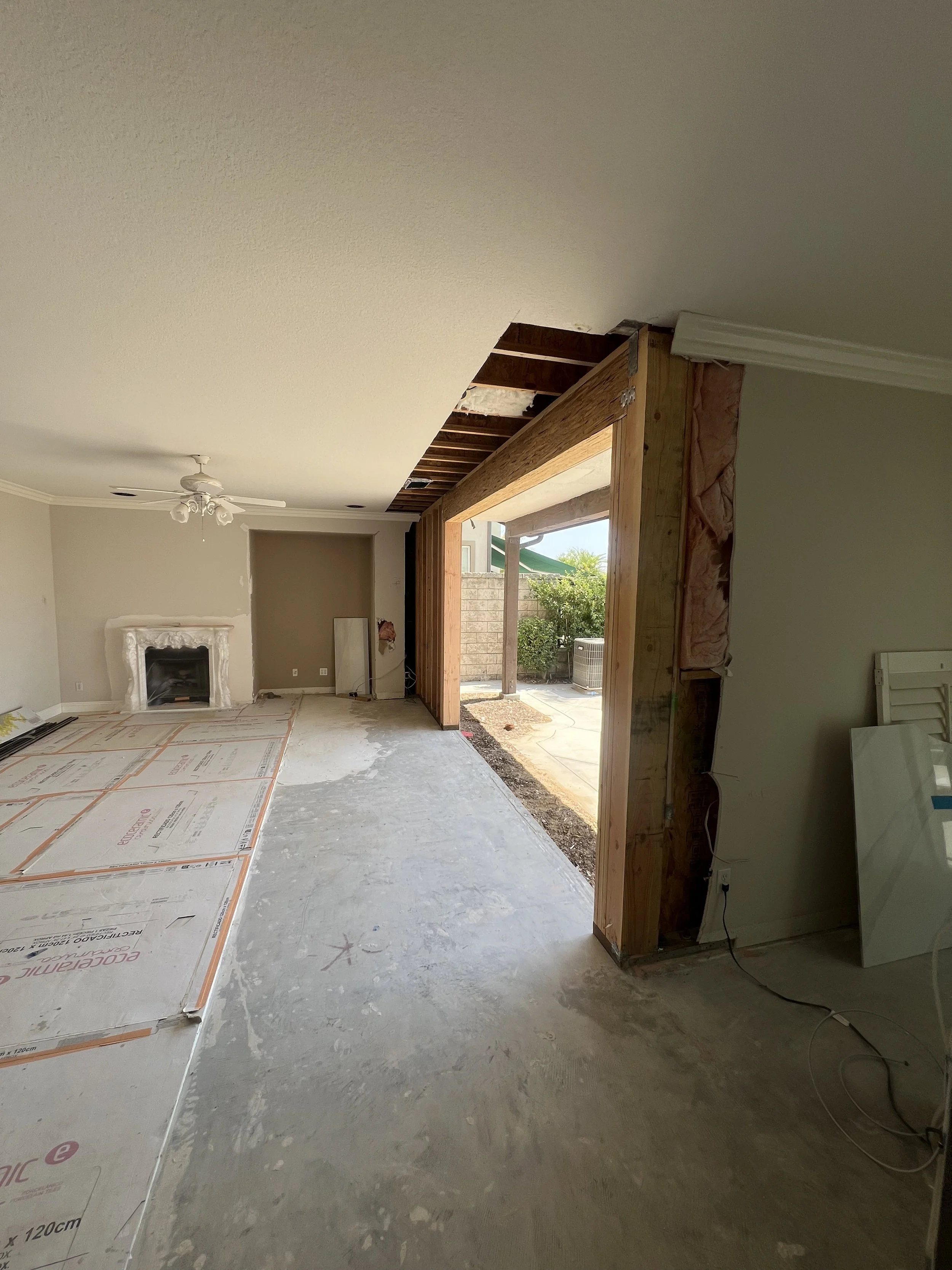 Living room with a fireplace, ceiling fan, and large doorway under construction leading to an outdoor patio.
