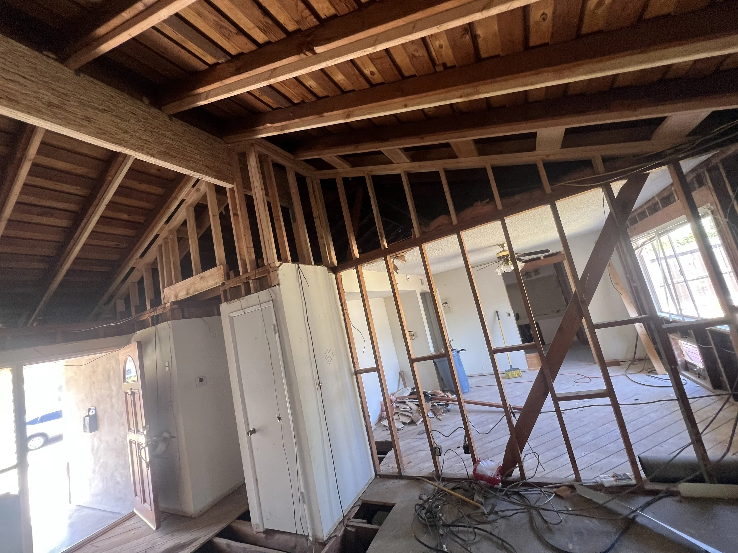 Interior of a house under renovation with exposed wood framing, wiring, and construction materials scattered on the floor.