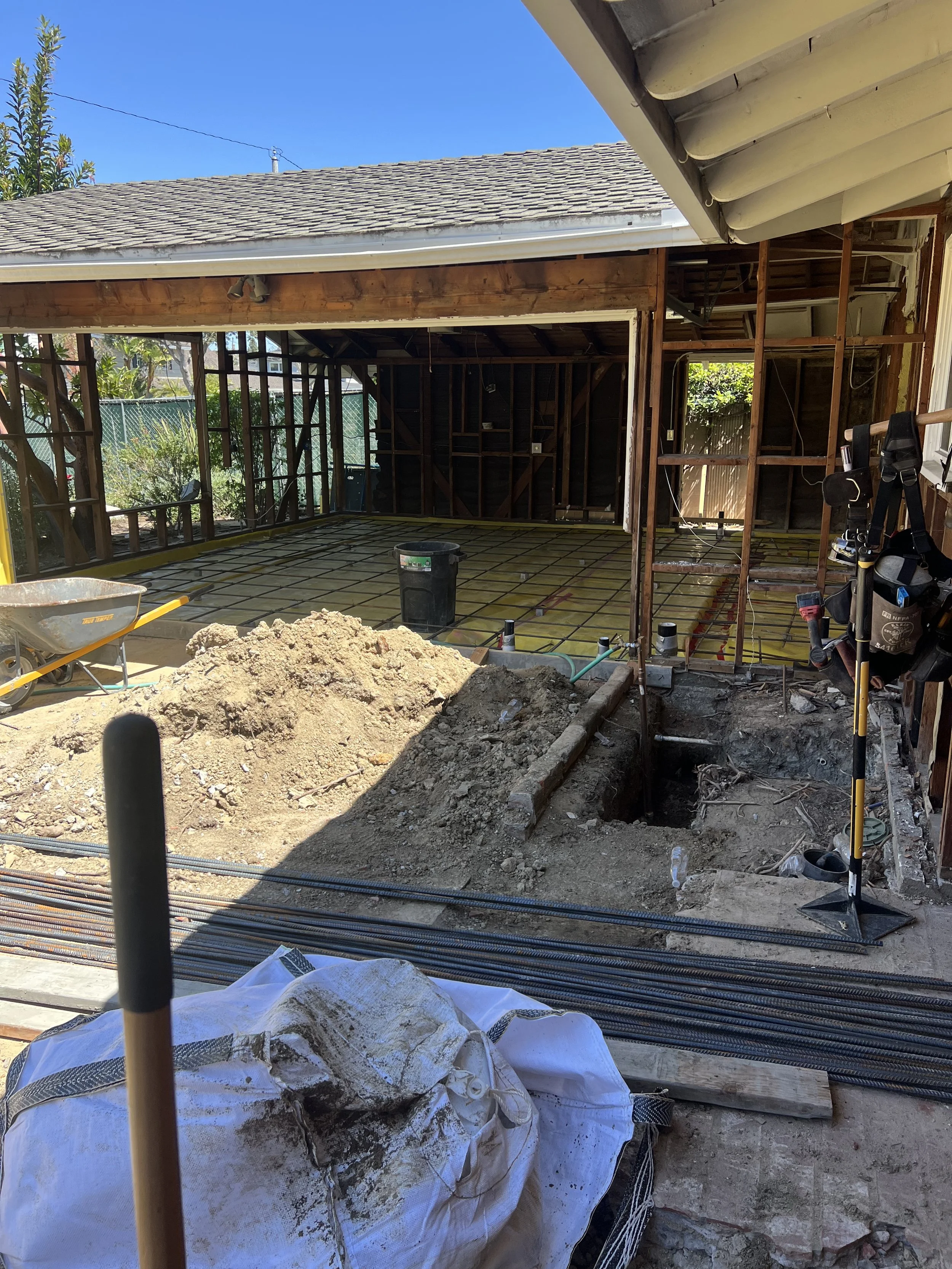 Construction site of a house renovation or addition, showing exposed wooden framing, rebar, and construction tools.