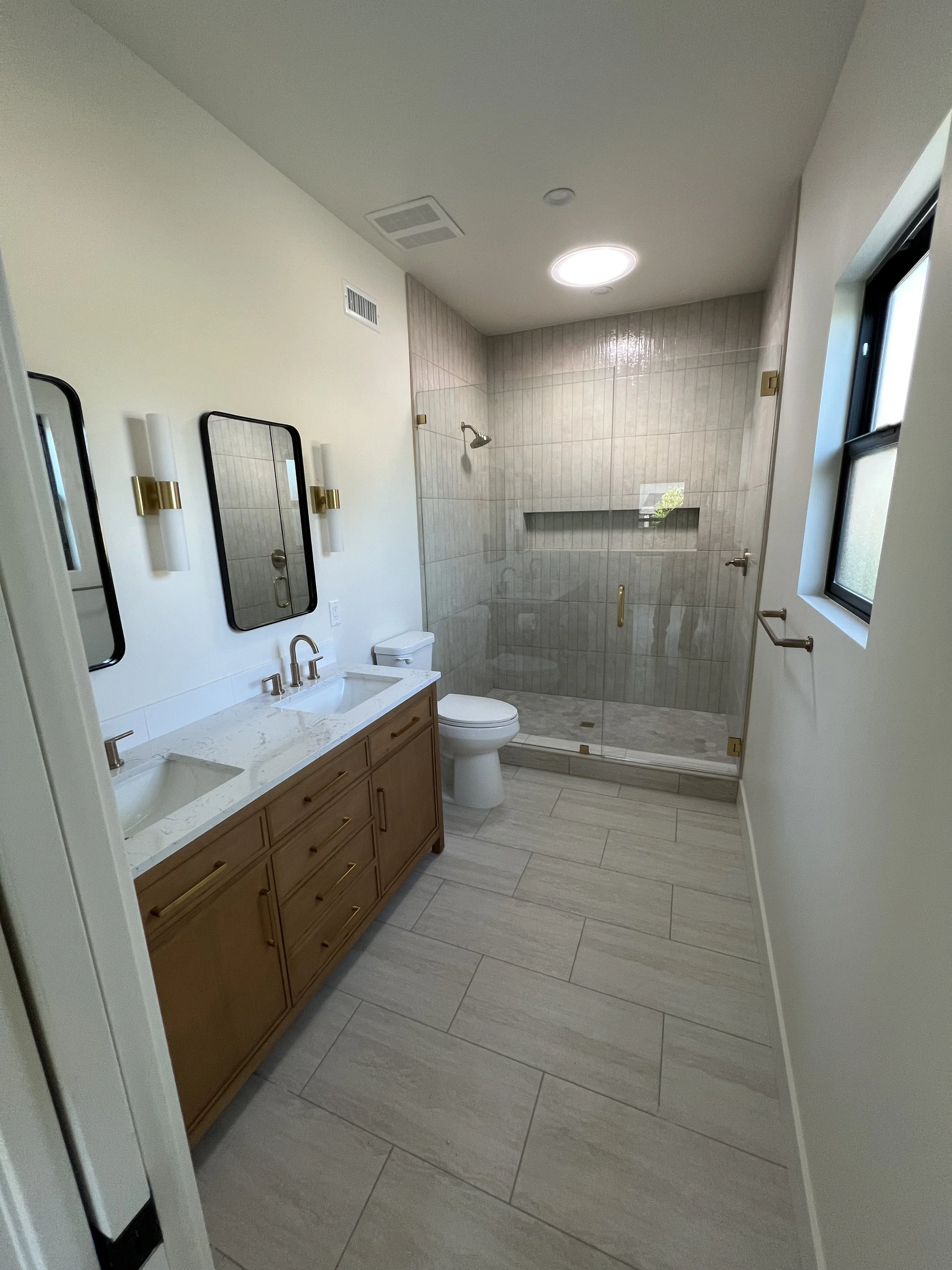 A modern building with wooden and white exterior walls and a large glass window, set against a backdrop of mountain terrain with dry grass and small trees in the foreground.