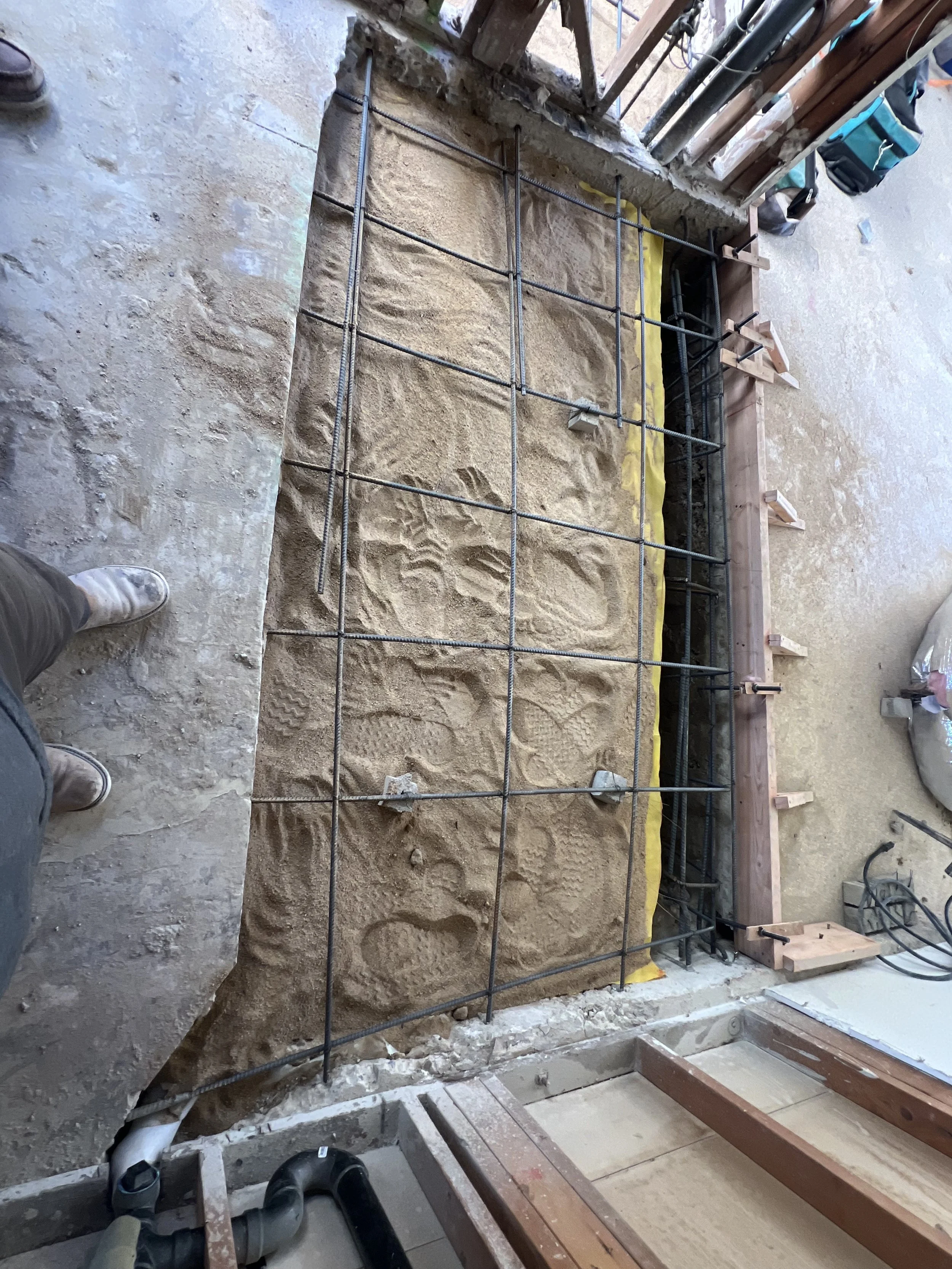 Construction site with rebar grid, sand, and wooden formwork for a concrete slab.