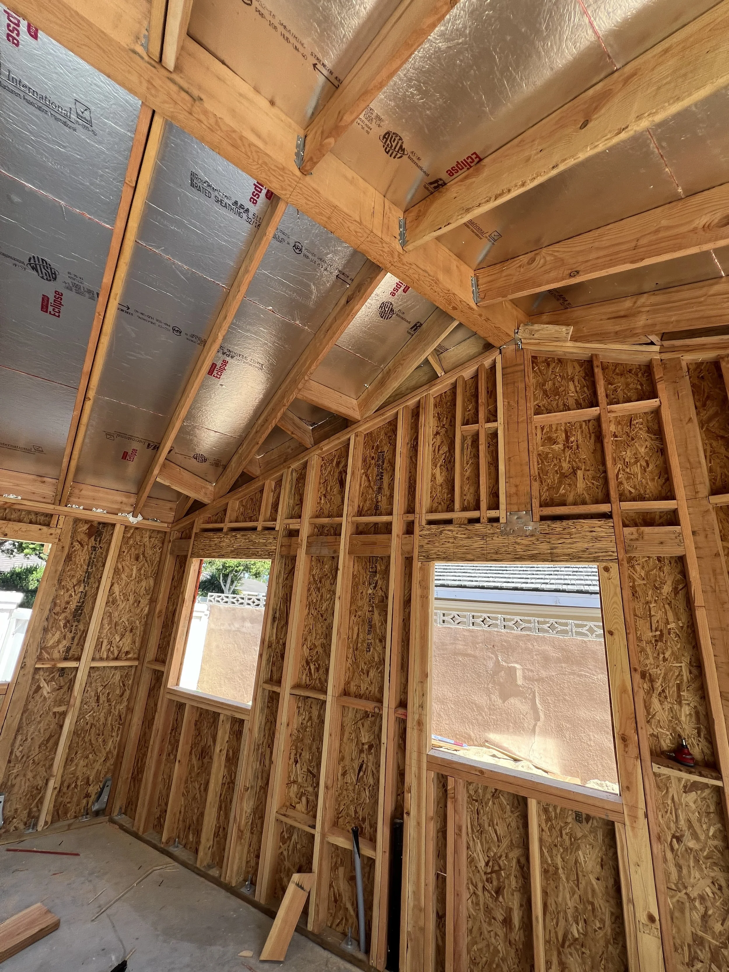 Wooden framing and insulation in a house under construction, with visible studs, joists, and open window spaces.
