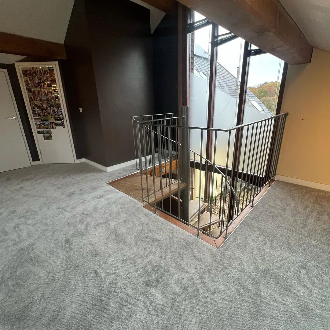 Interior view of a room with gray carpet, a spiral staircase down, large windows, and a collage of photos on a white door.
