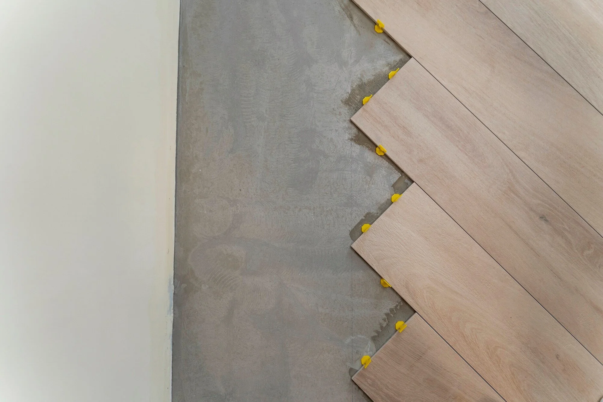 Close-up of a partially tiled floor showing yellow spacers between wood-look tiles and an unfinished concrete section.