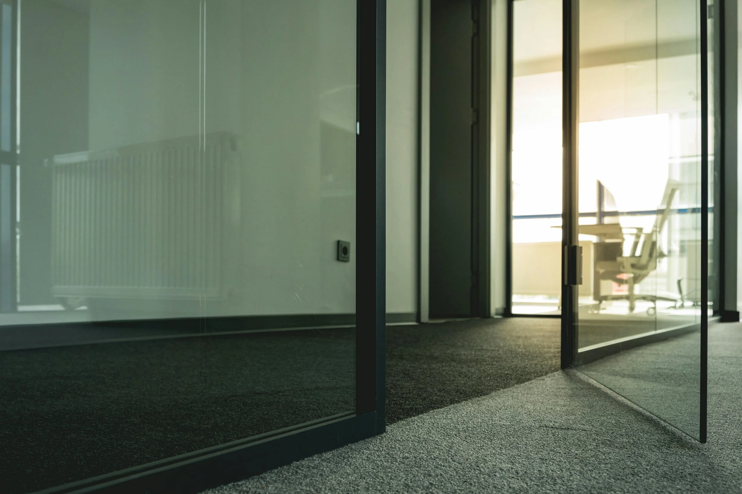 Office interior with glass walls and door, view of a desk and chair through the glass
