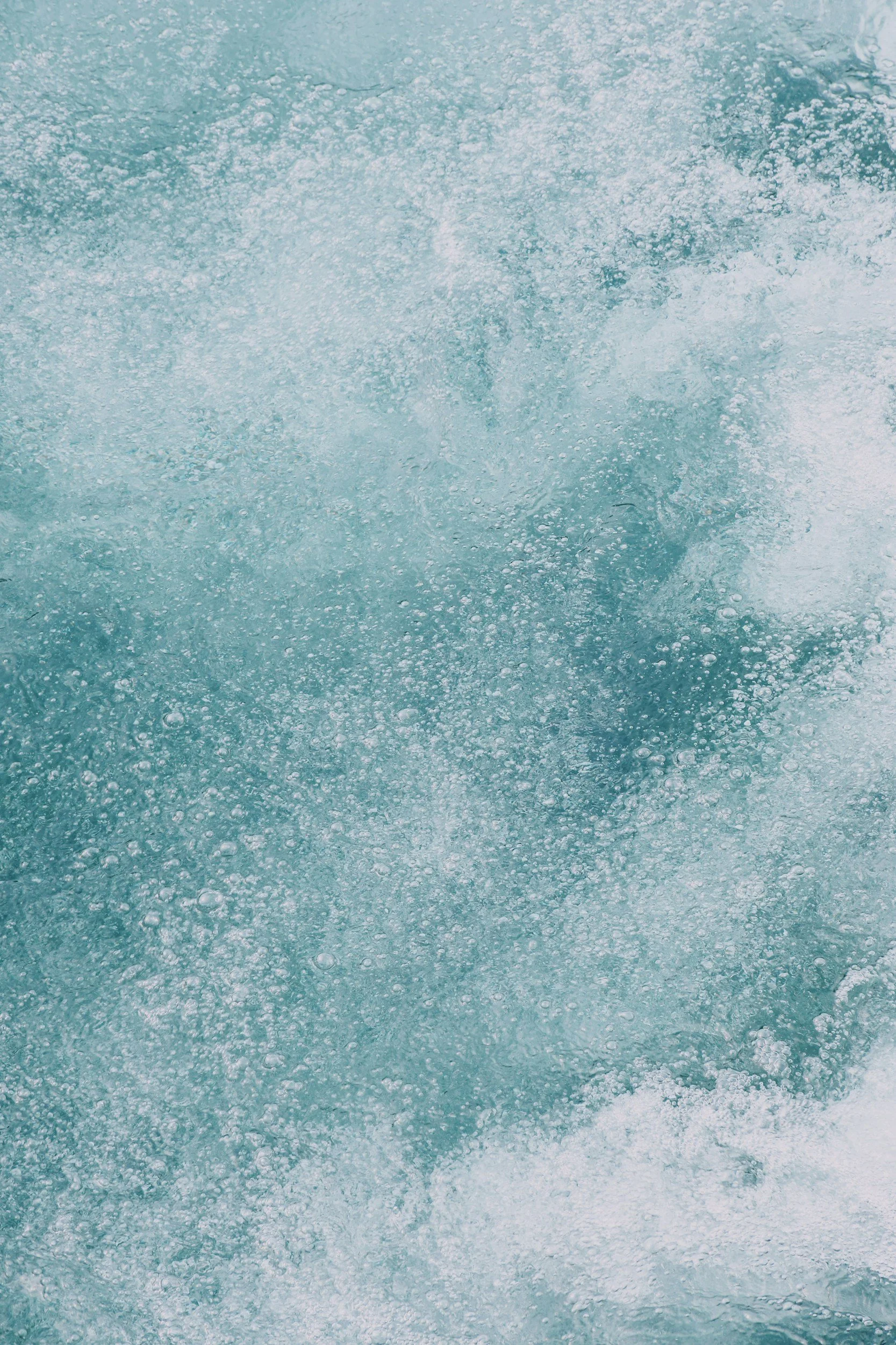 A close-up of turbulent blue ocean water with white foam and bubbles.