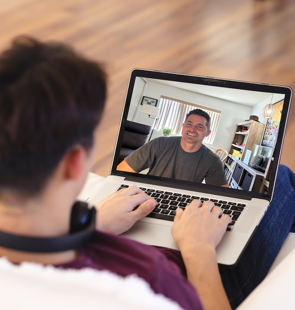 Person with headphones using a laptop to video chat with a man smiling on the screen