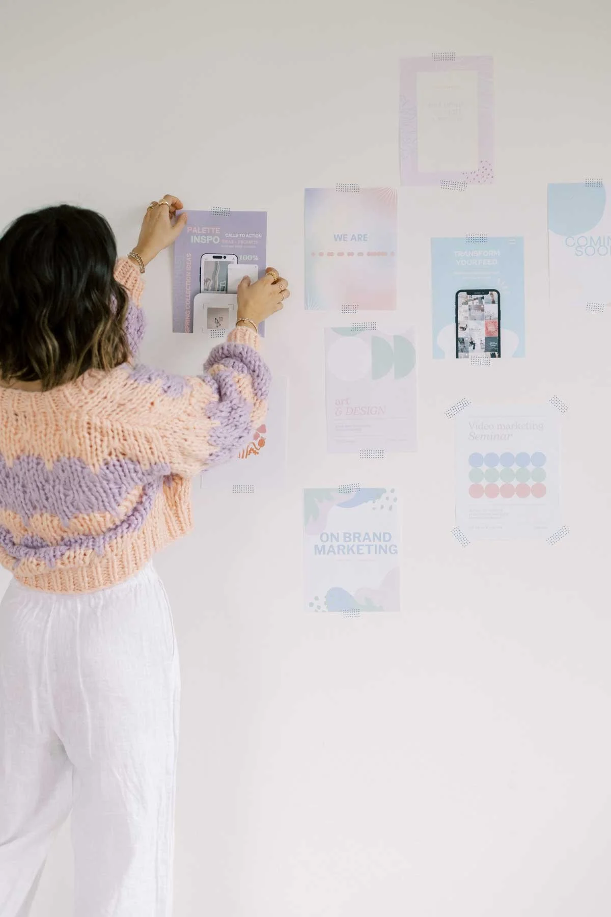 A woman in a soft, creative workspace pins pastel brand visuals to a wall as part of a visual alignment and brand strategy process.