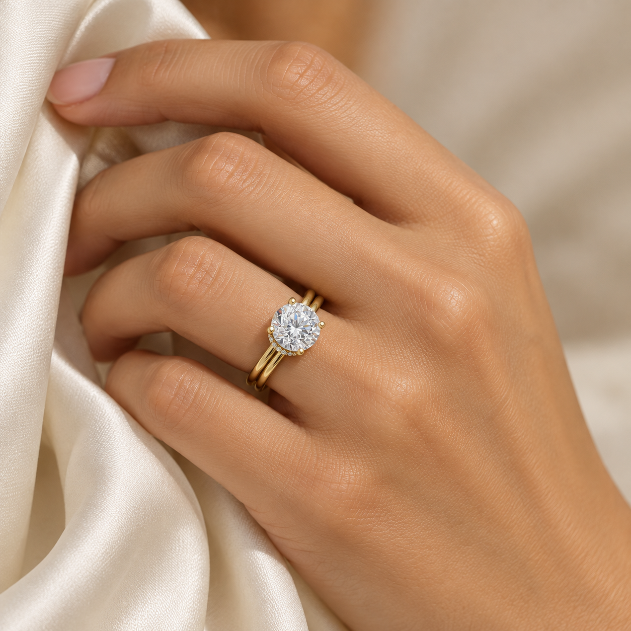 Yellow gold Vela Hidden Halo Ring worn on a hand holding ivory silk.
