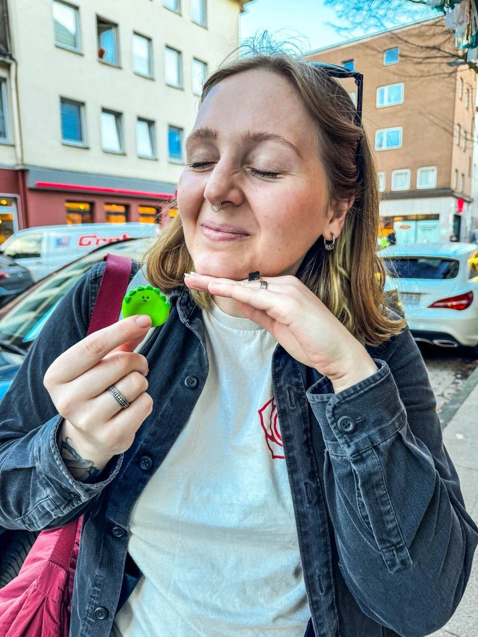 Junge Frau mit geschlossenen Augen, hält einen grünen Fidget-Spinner und lächelt auf einer Stadtstraße.