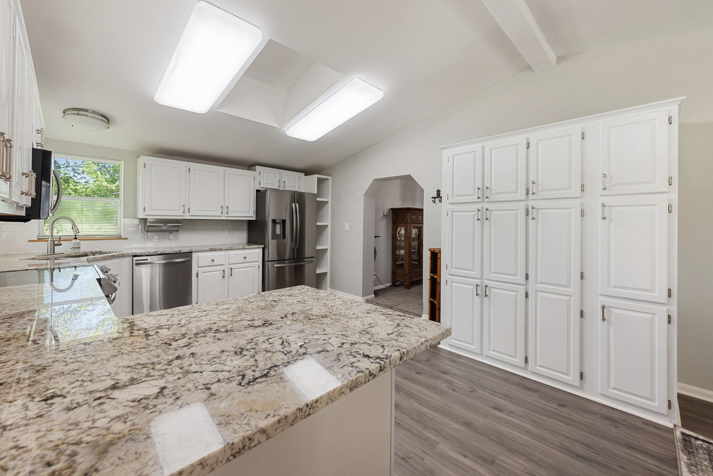 Modern kitchen with white cabinets, granite countertops, stainless steel appliances, a window, and light gray wood flooring.