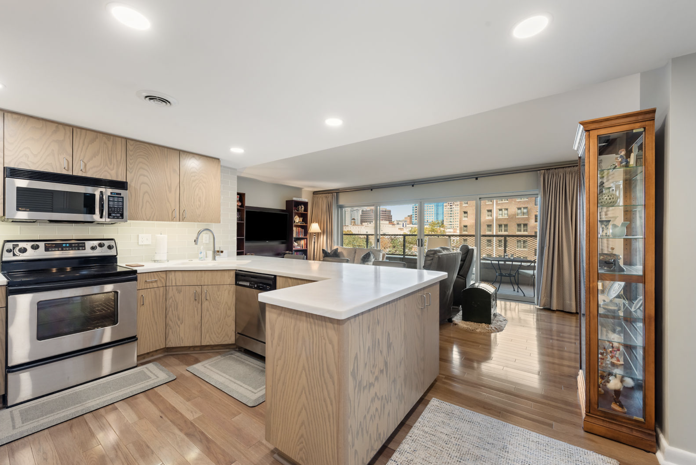 Open-concept kitchen and living area with wooden cabinets, stainless steel appliances, and a balcony with city view.