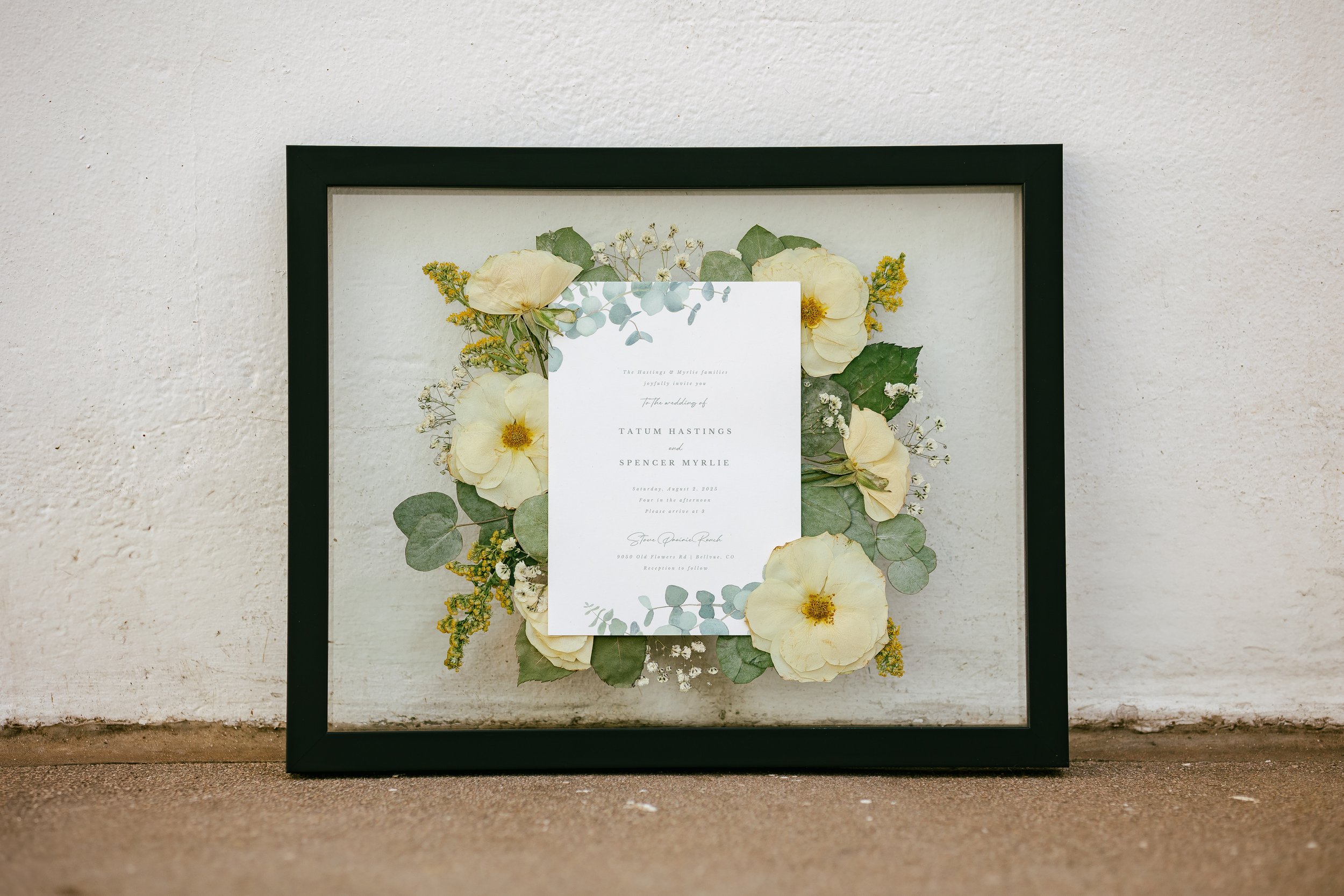 A pressed floral frame that includes a bouquet in the center, surrounded by white and green florals.