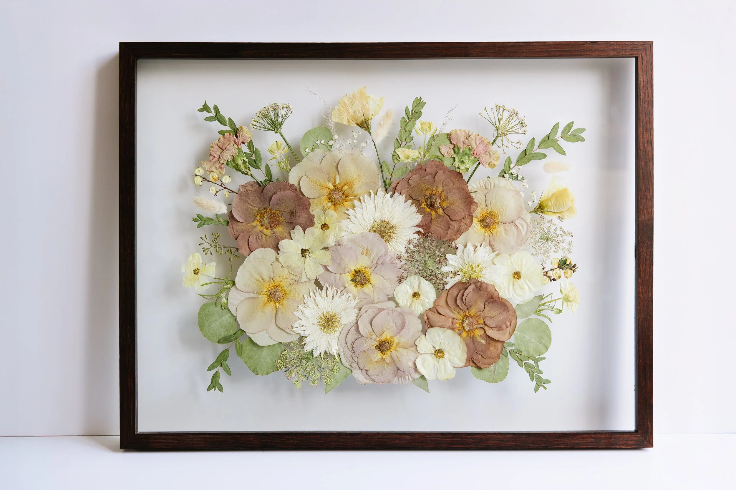 A pink and brown bouquet is framed in a brown frame.