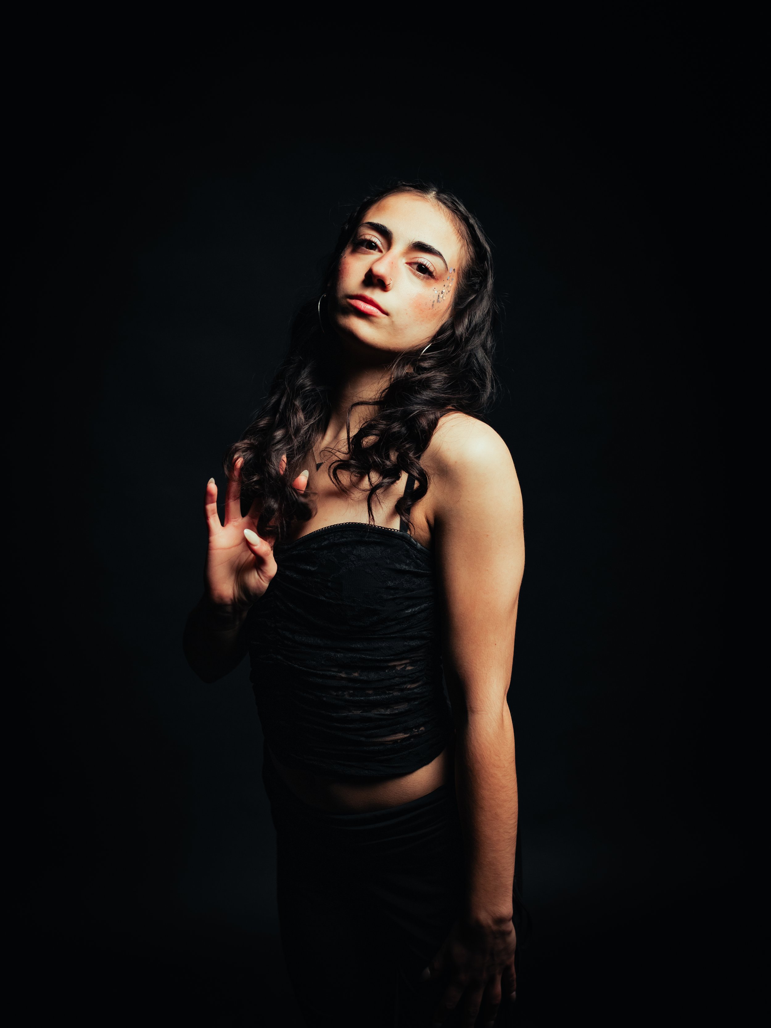 Young woman with long dark hair wearing a black dress standing against a red background.