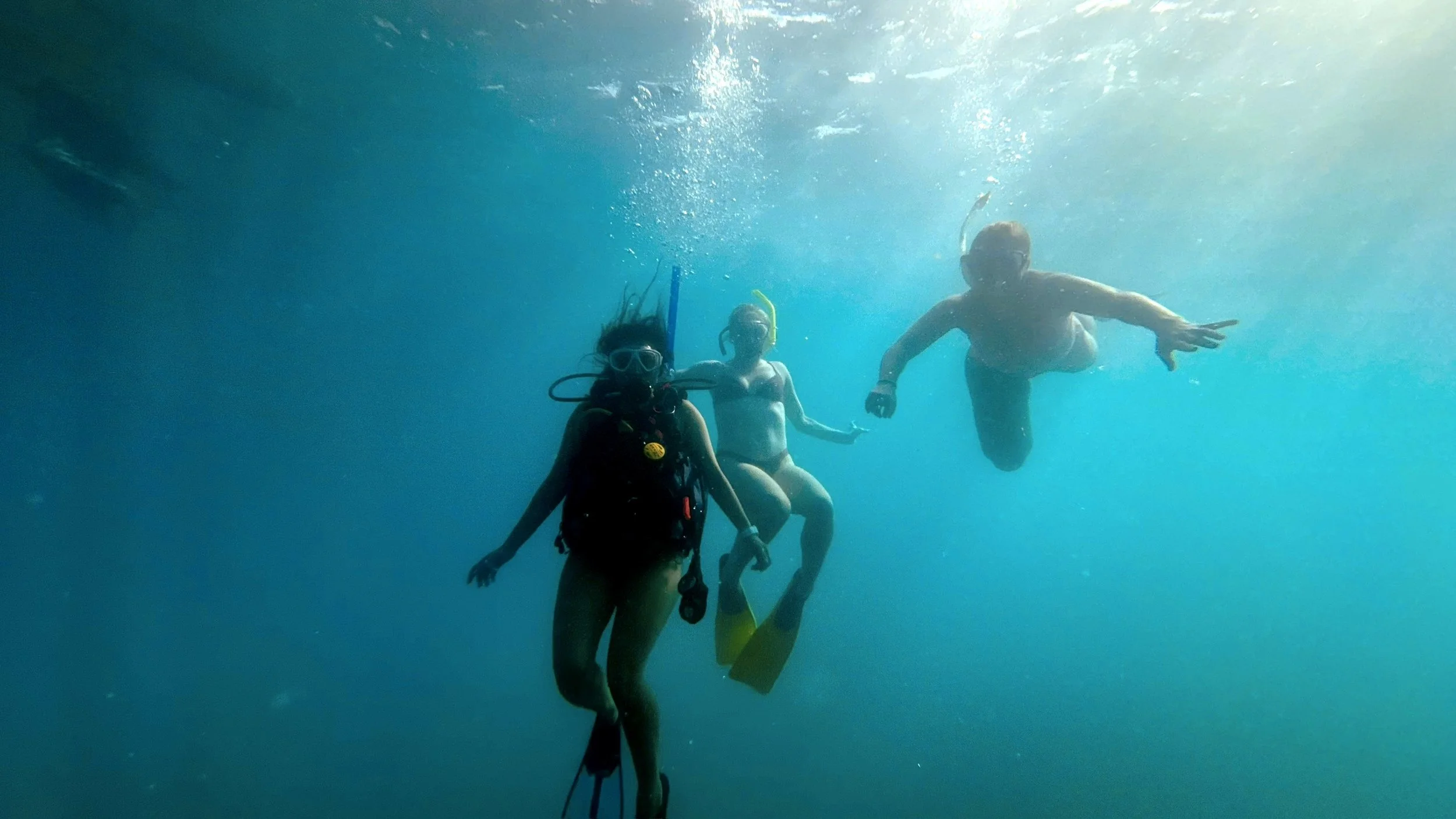 Three people scuba diving underwater, wearing masks and fins.