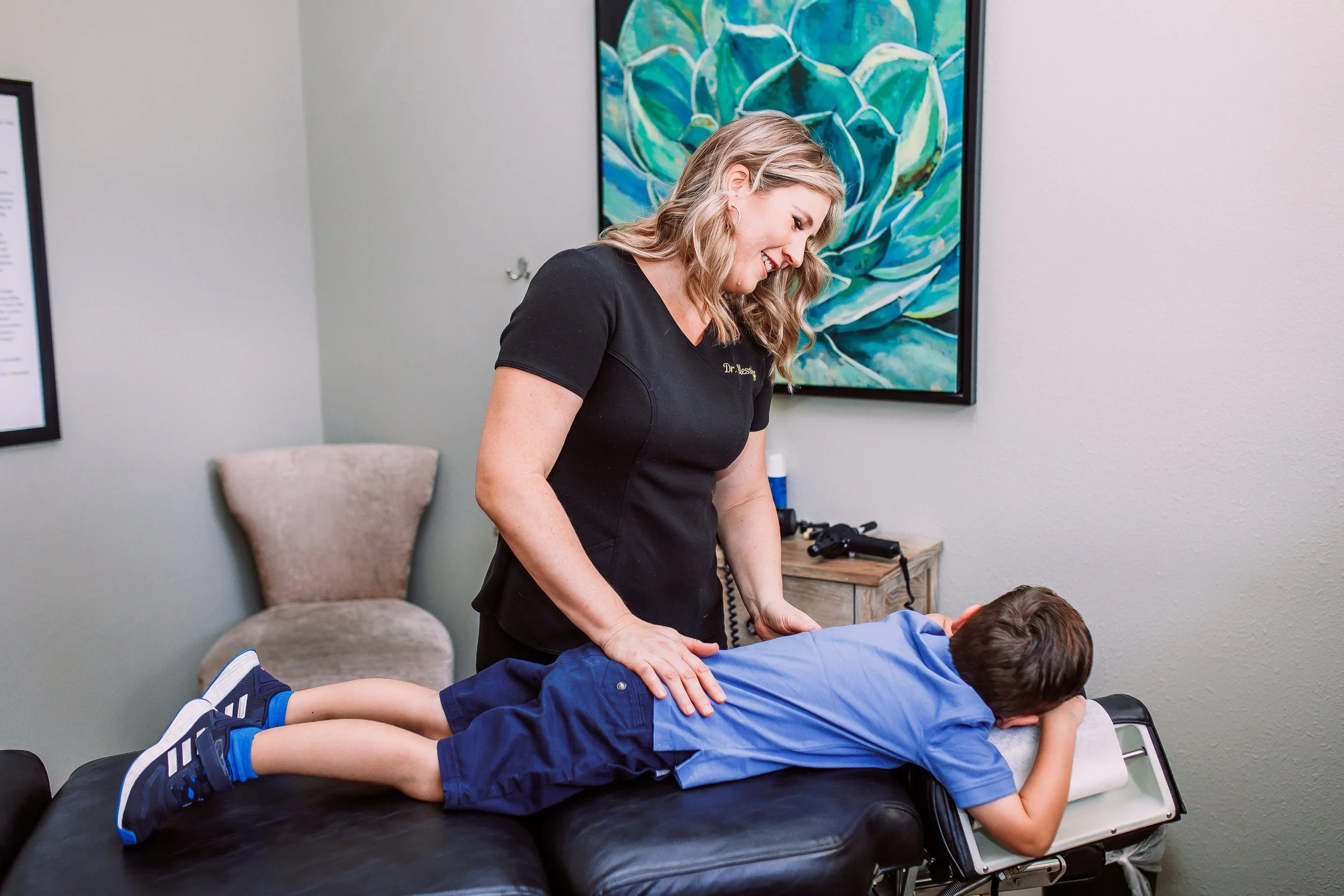Medical professional performing a spinal examination on a young boy lying face down on a treatment table in a well-lit room.