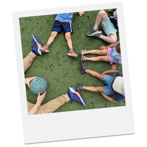 Group of children sitting and lying on artificial grass, playing with a small globe and a ball outdoors.