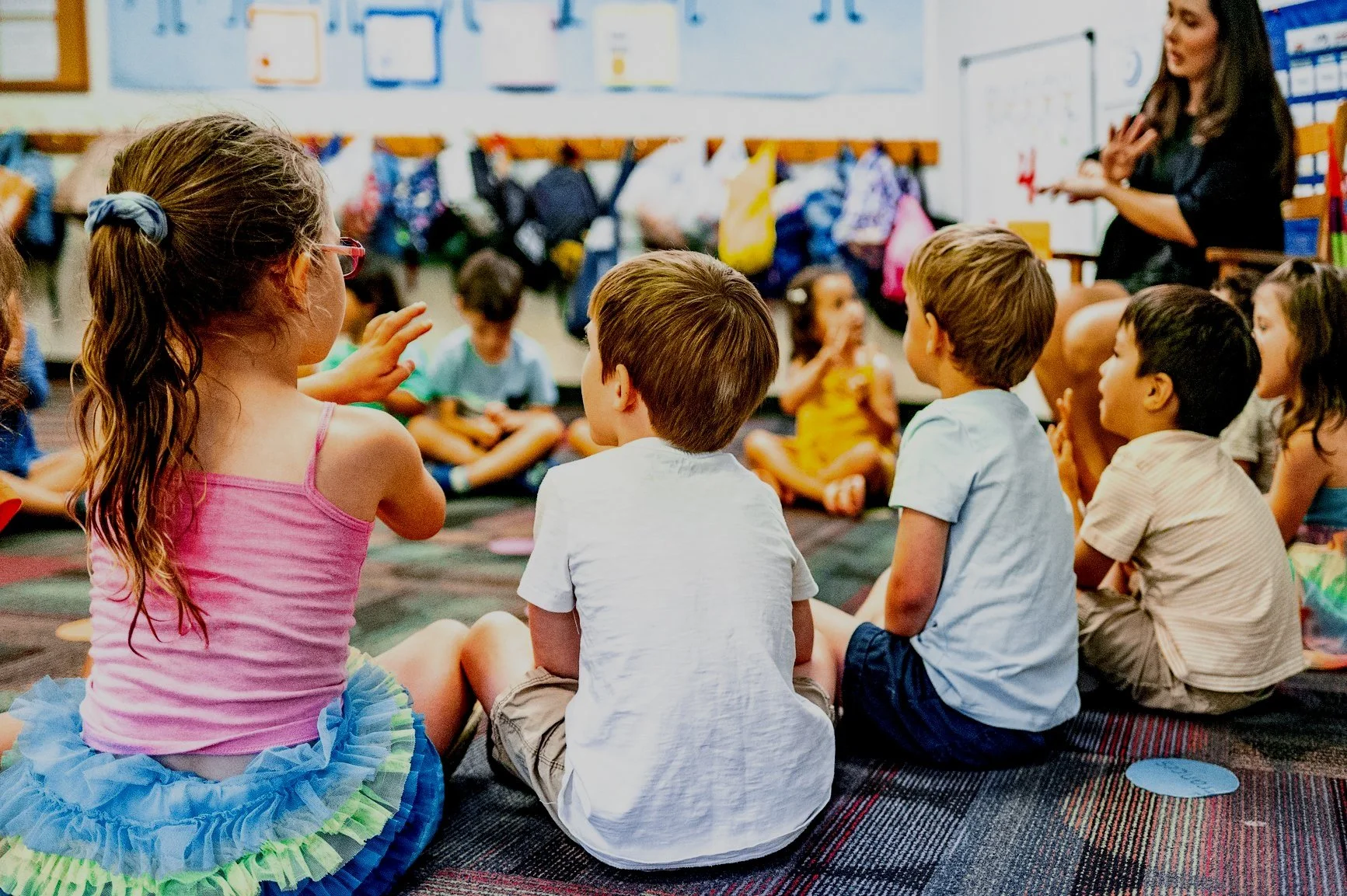 Children sitting in a circle during a classroom activity, with a teacher guiding them.