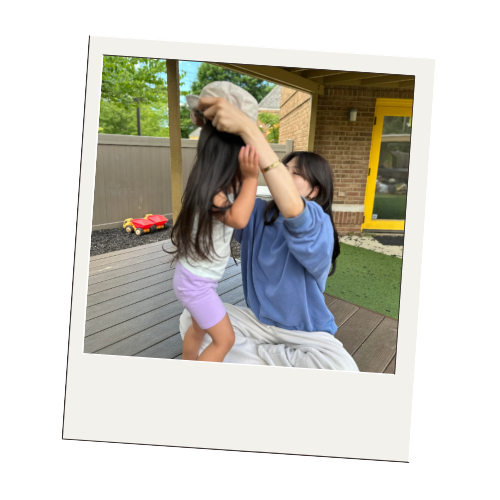 A woman and a young girl play on a porch with a stuffed animal.