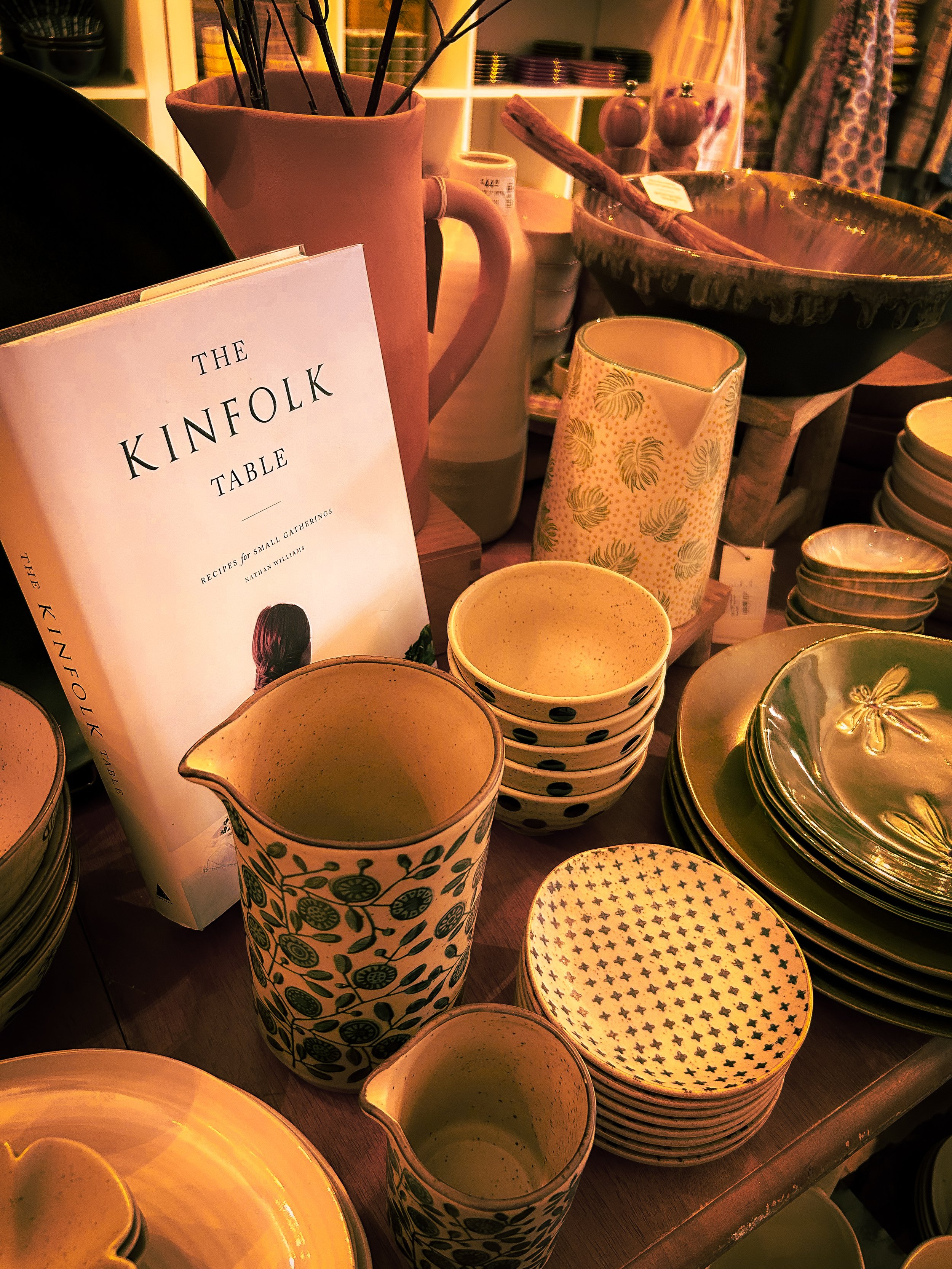 Display of ceramic dishes, bowls, and pitchers alongside the book 'The Kinfolk Table.'