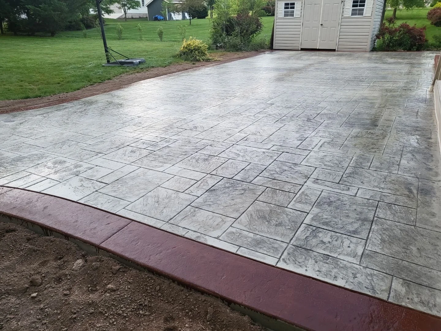 Finished gray stamped concrete patio with a red decorative border, backyard lawn view