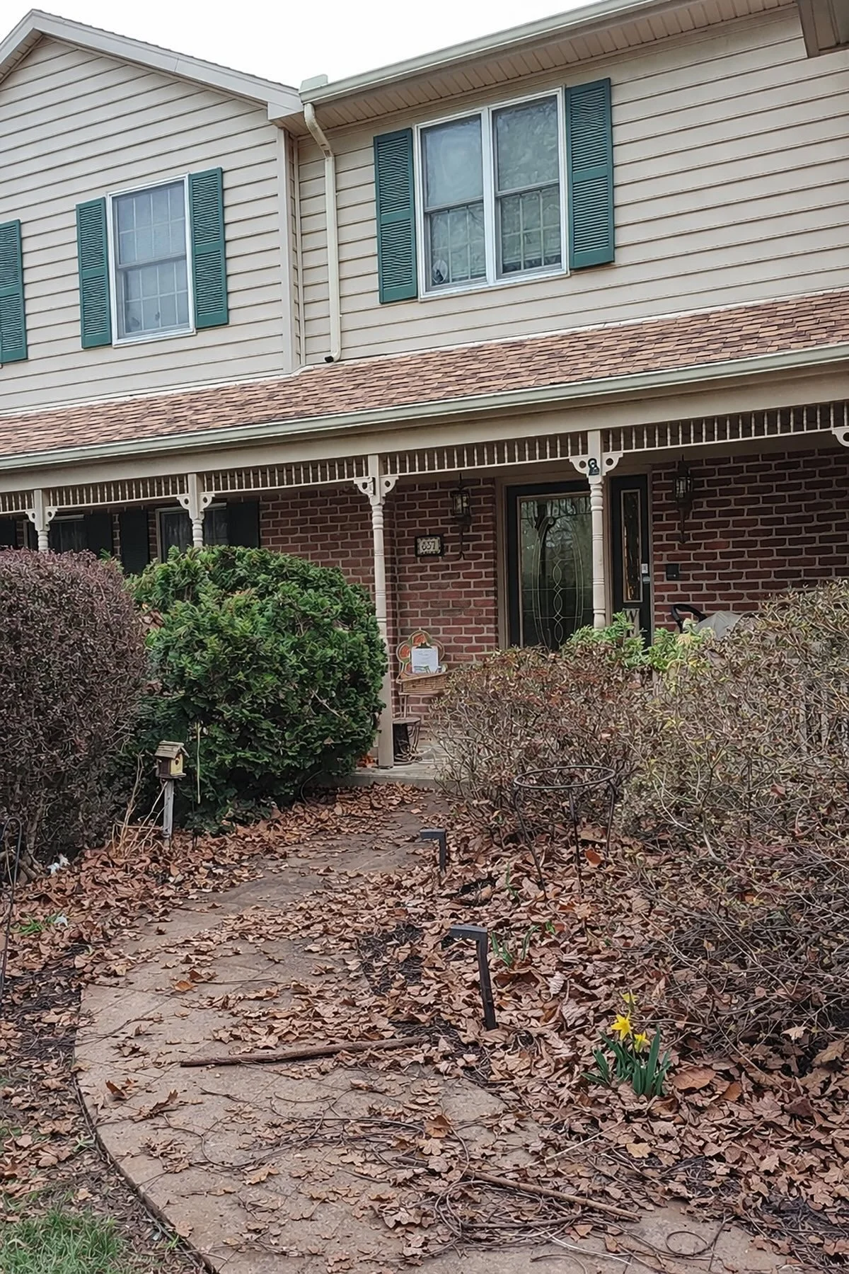 Overgrown front walkway and garden bed covered in leaves and debris before spring cleanup service in Central Pennsylvania