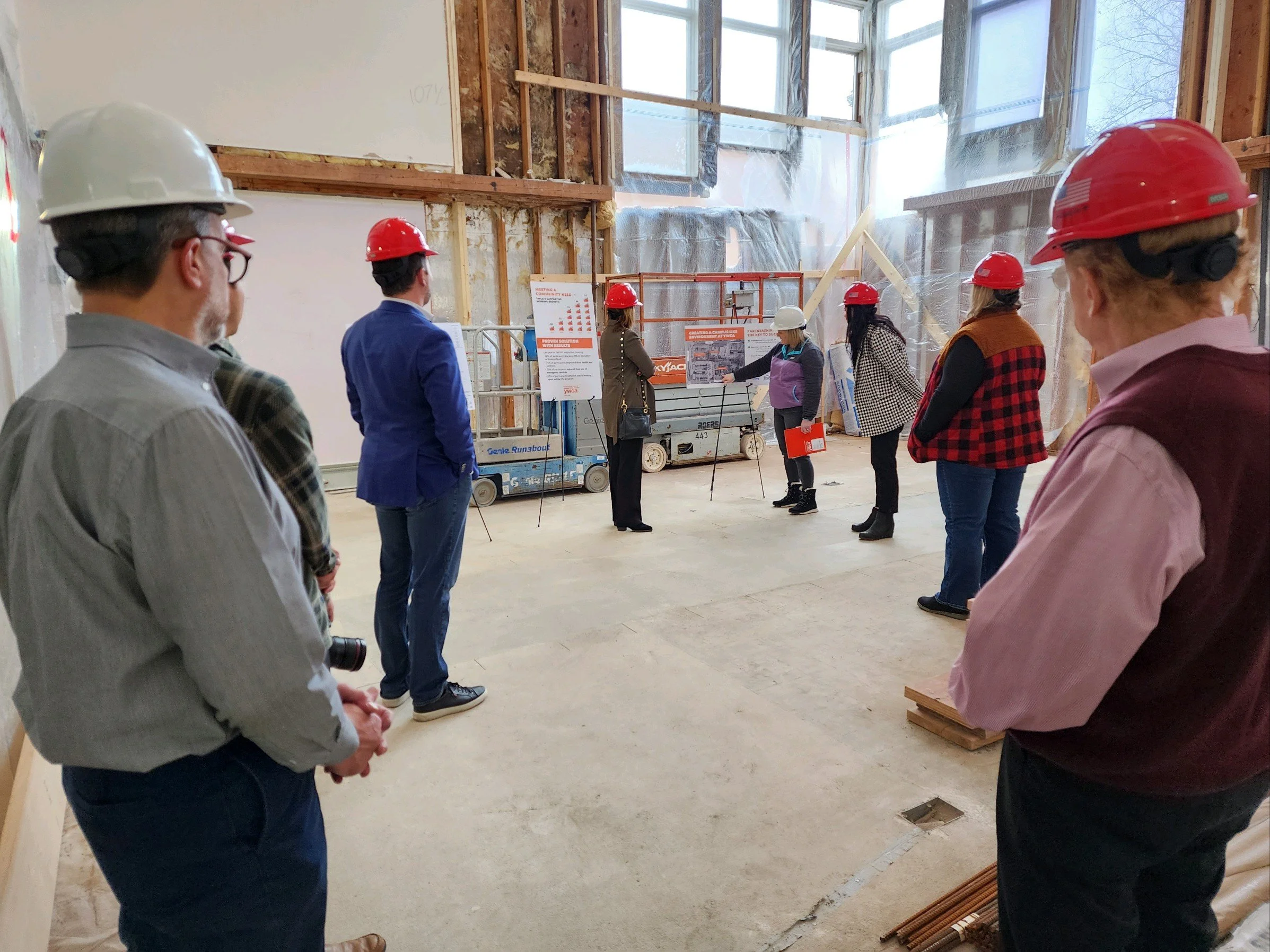 Group of people wearing hard hats and standing in an unfinished building during a construction presentation or tour.