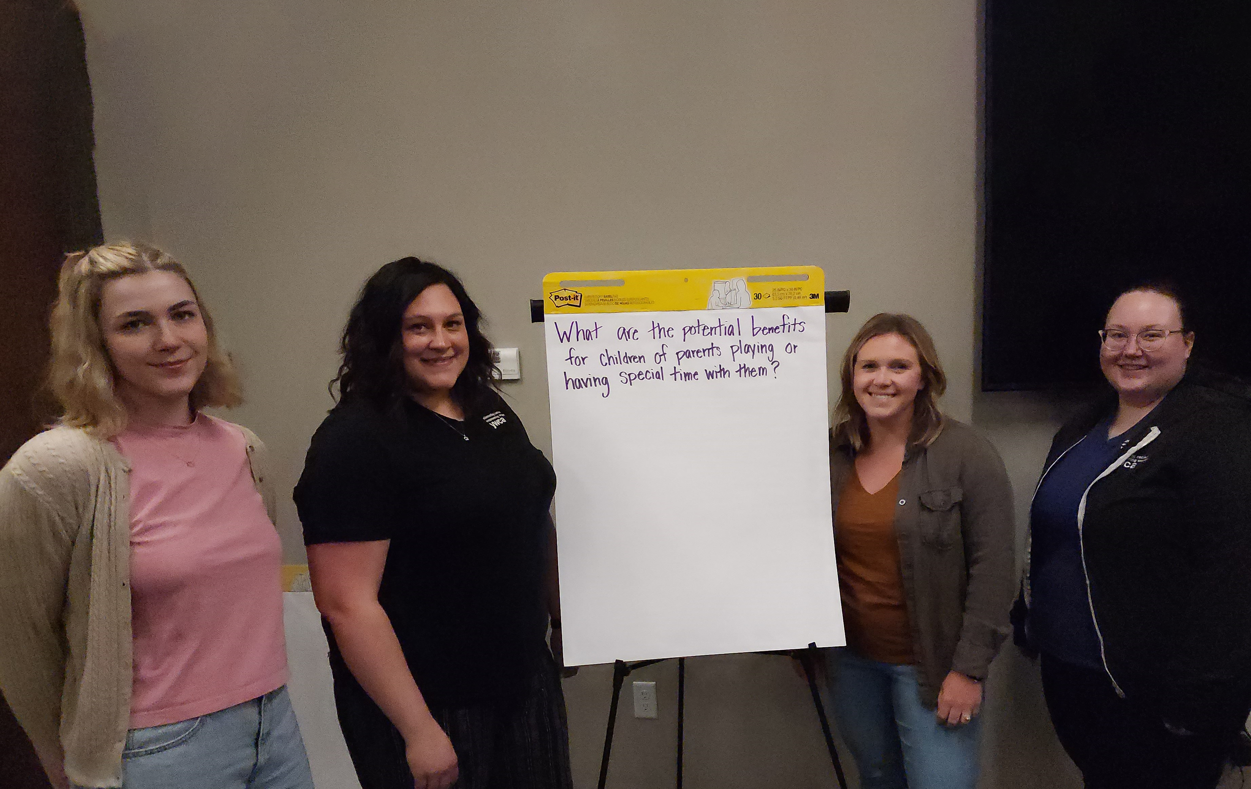 Four women stand next to large pad of paper