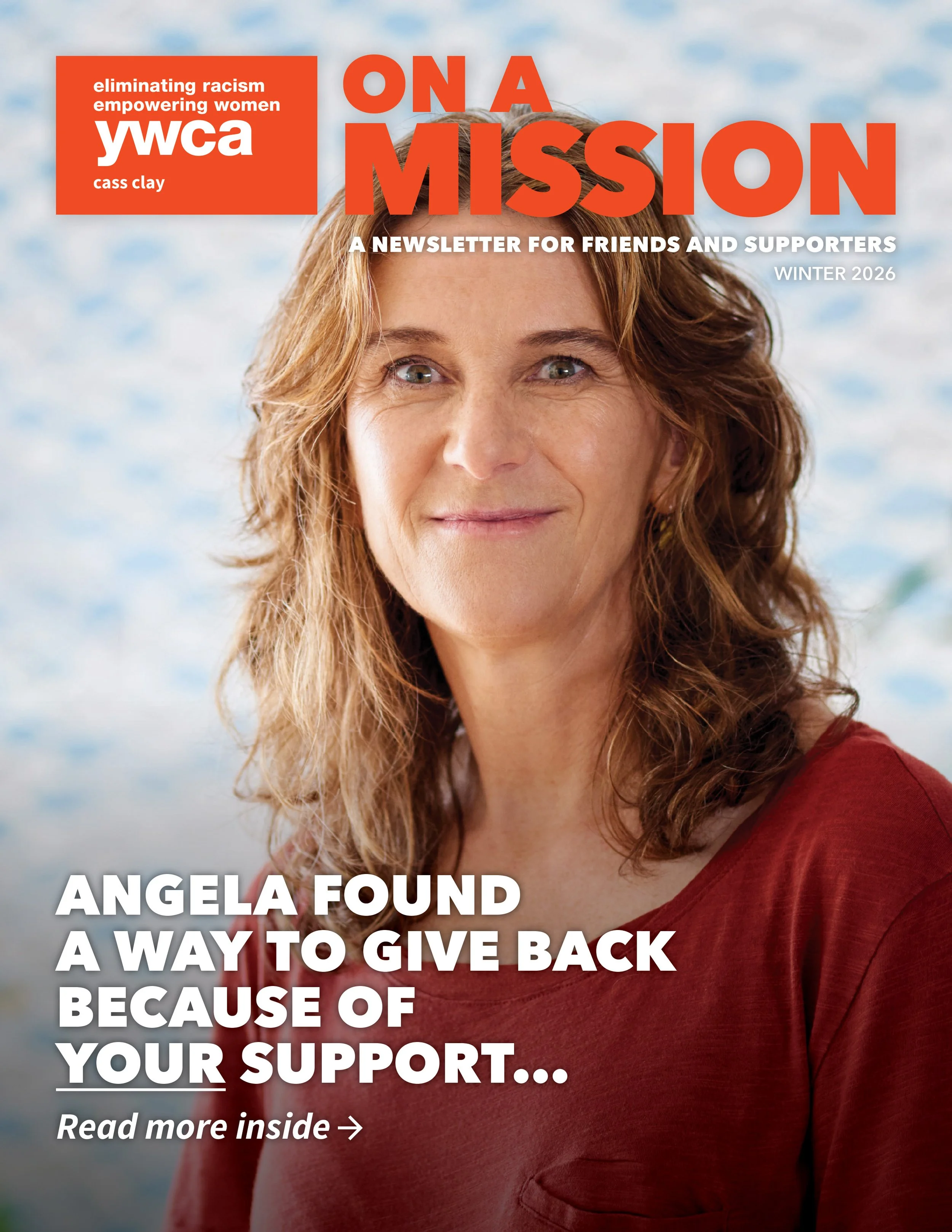 White woman with curly red-brown and red shirt smiling in front of white and blue blurred wallpaper
