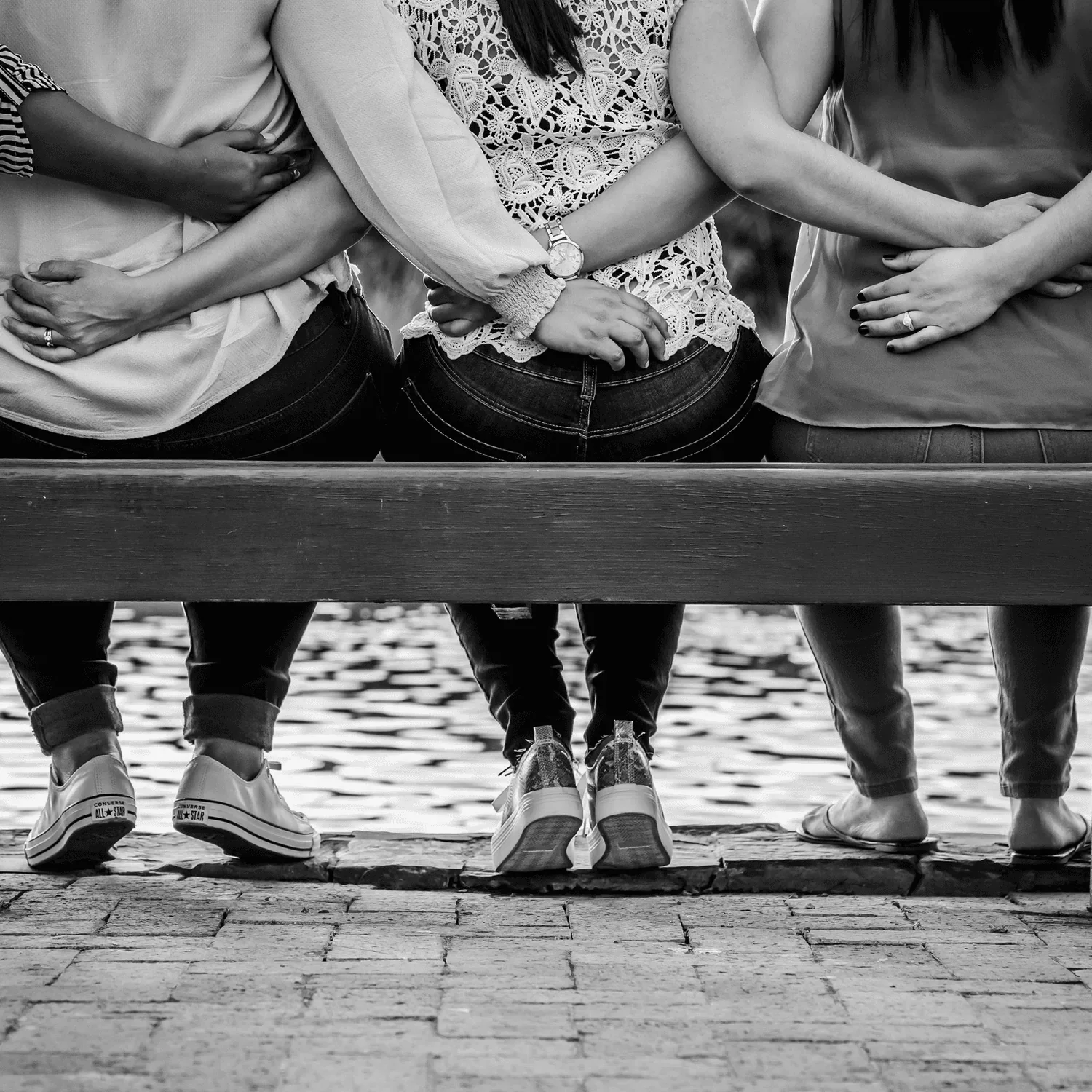 Three women sitting on bench holding each other in black and white portrait