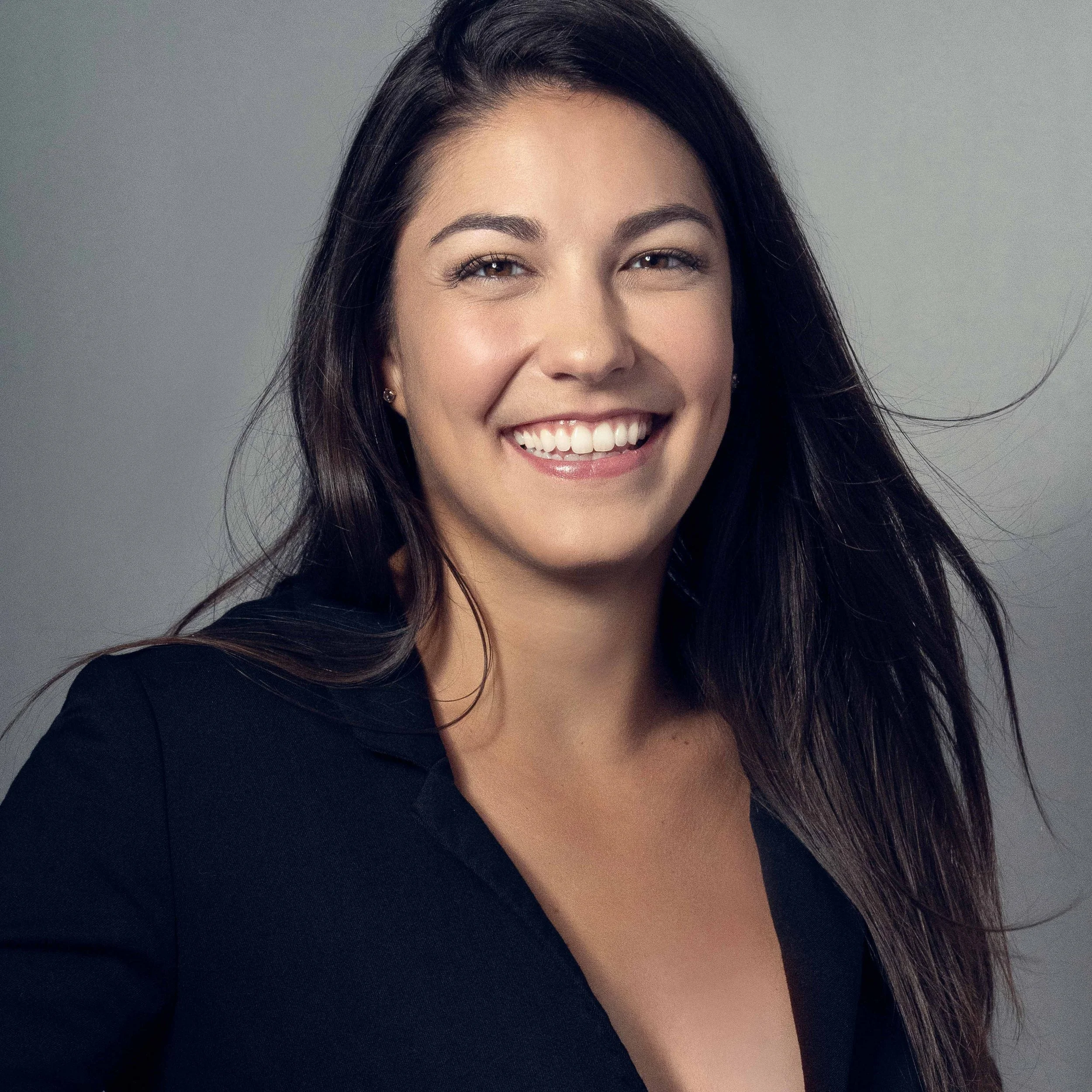 brunette woman with a dark blue blazer on a grey background - portrait playdate