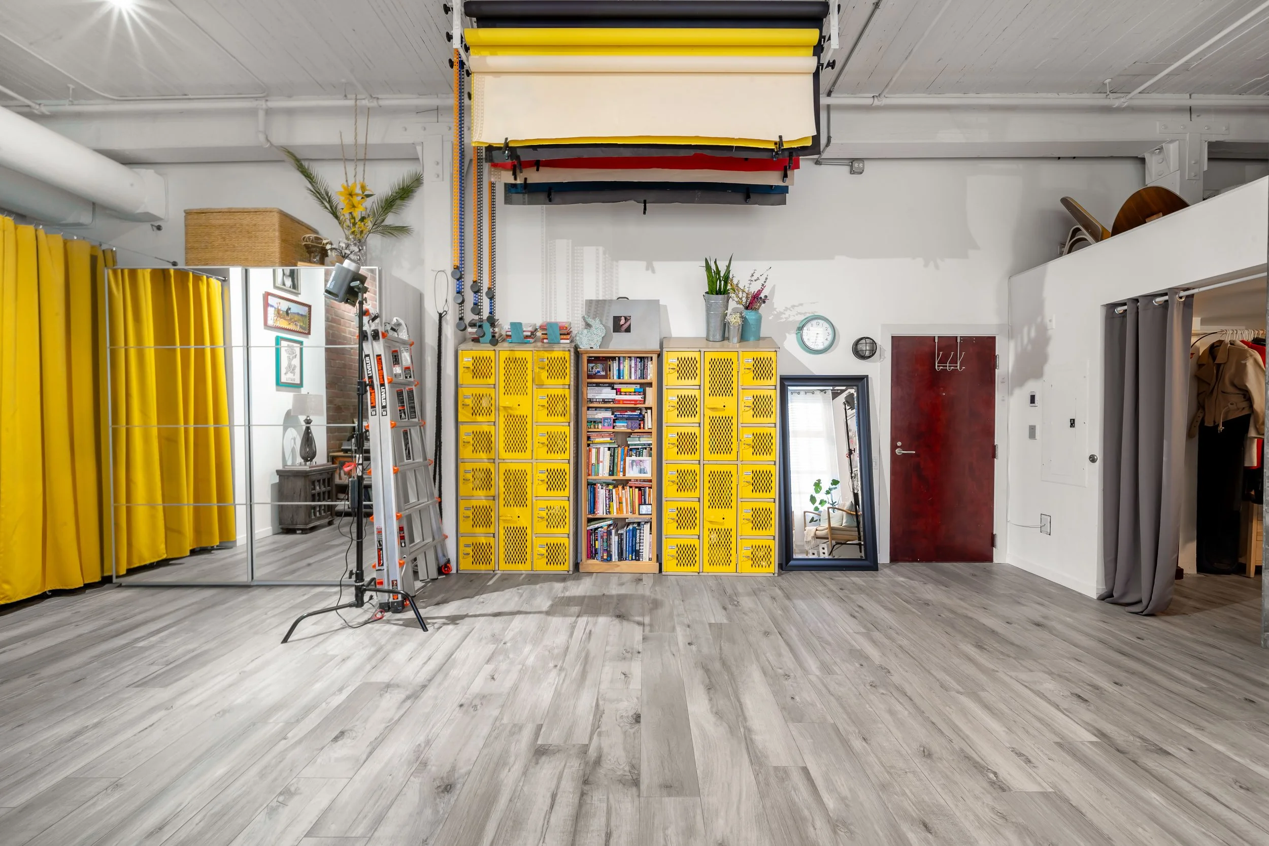 The interior of the Portrait Playdate headshot and portrait photography studio in Seattle, WA, with yellow lockers, a large mirror, bookshelves, and colorfully layered backdrops on the ceiling, along with various decorations and equipment.