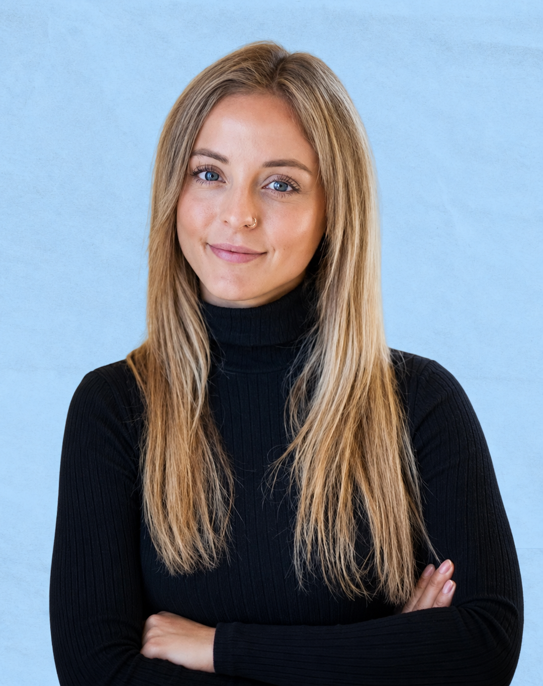 A young woman with blonde hair, blue eyes, and a nose ring, wearing a black turtleneck sweater, standing against a light blue background.