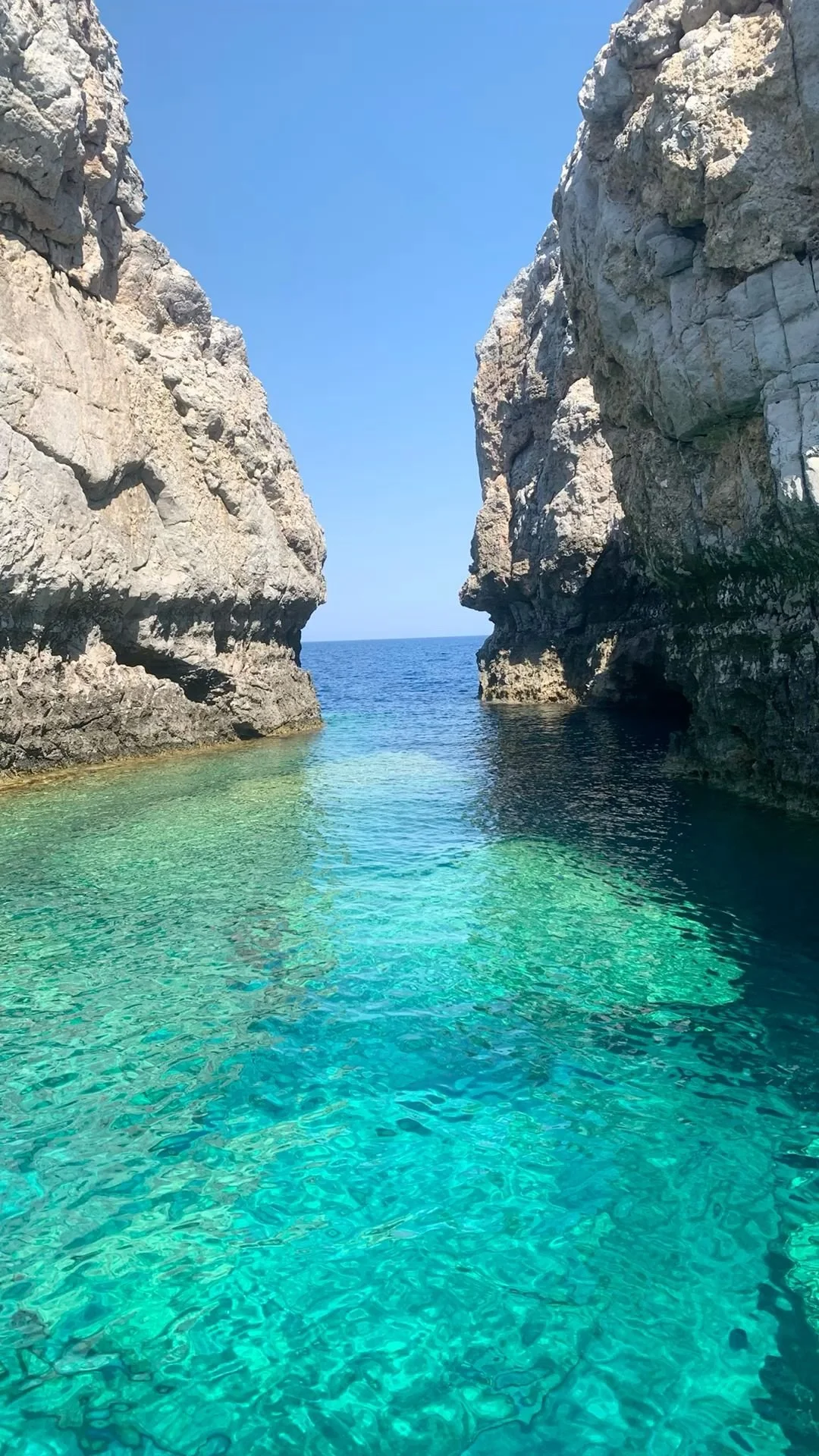 Rock formations on either side form a small passageway leading to the ocean, with clear turquoise water and a bright blue sky overhead.