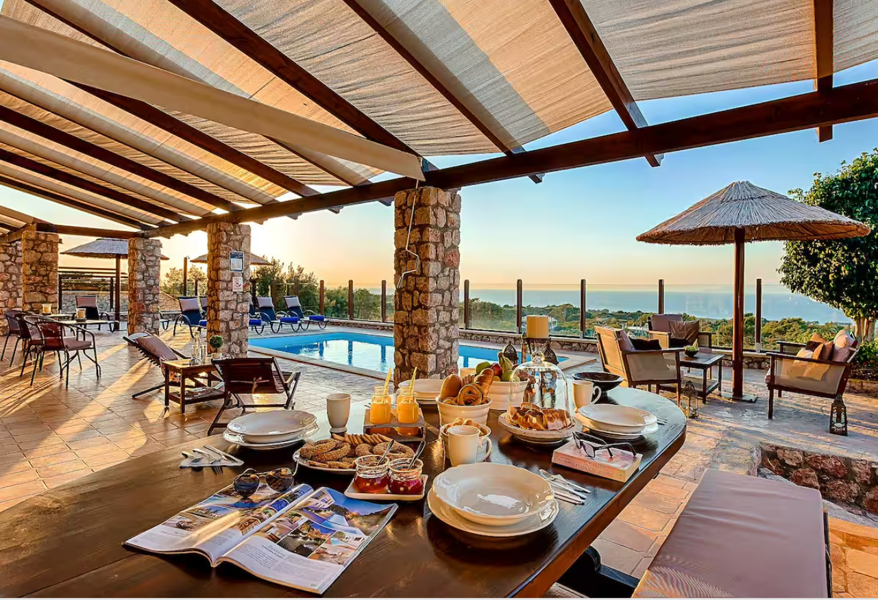 Outdoor patio with a breakfast table, pool, and a scenic view of the ocean at sunrise.