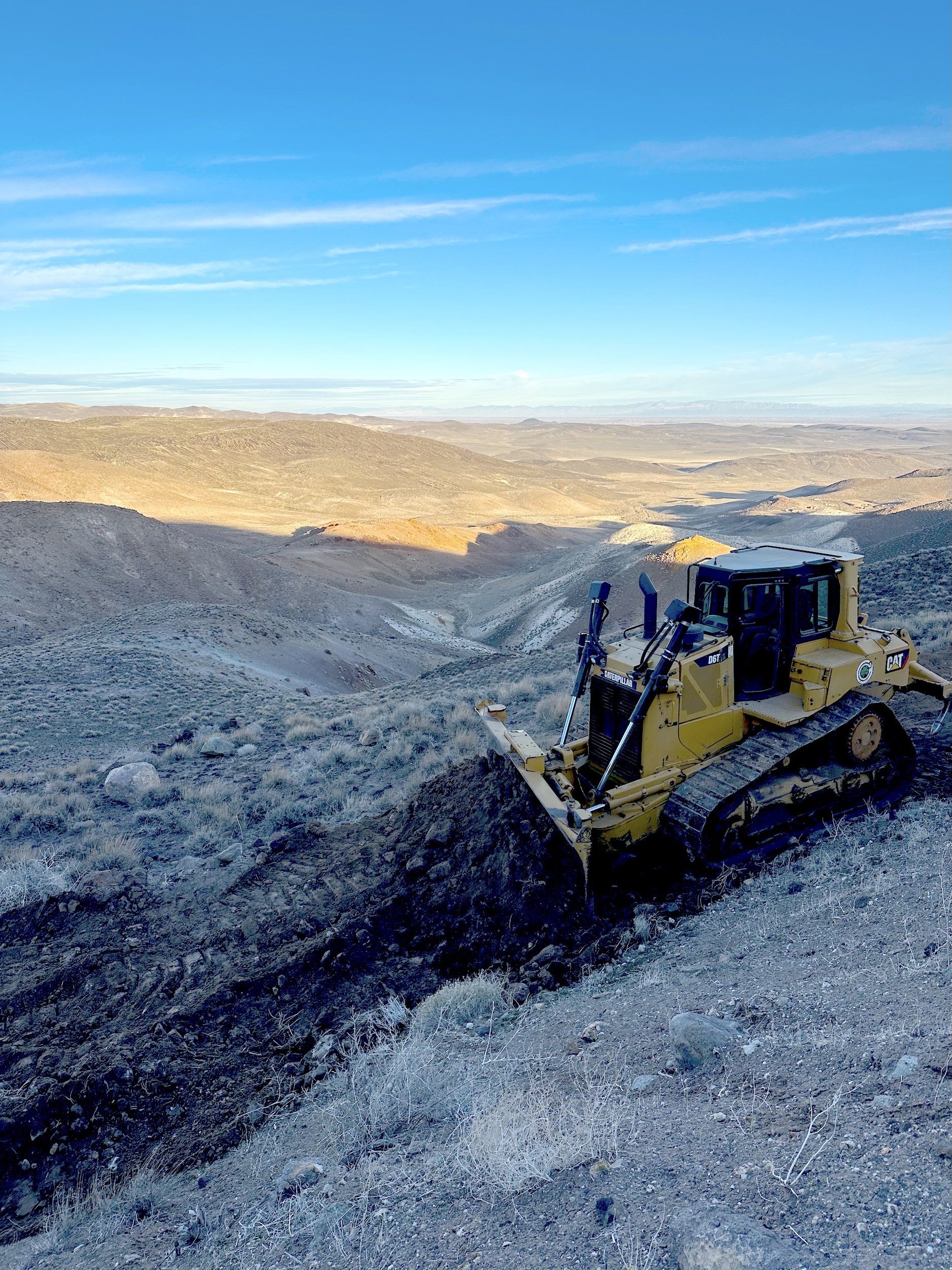 Bulldozer on a frosty hillside overlooking a valley at sunrise