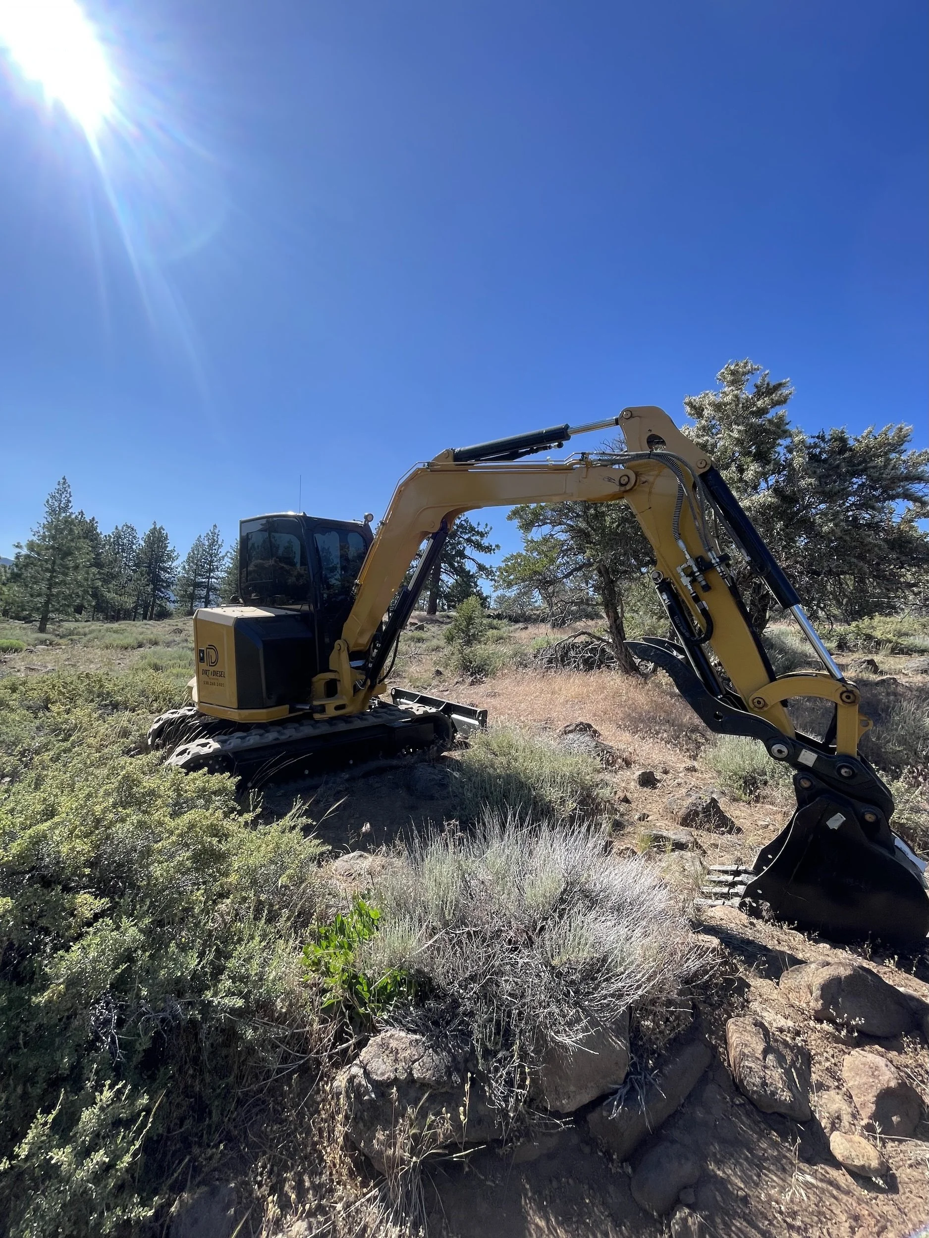 Excavator with a bucket clearing a brushy hillside in Northern Nevada