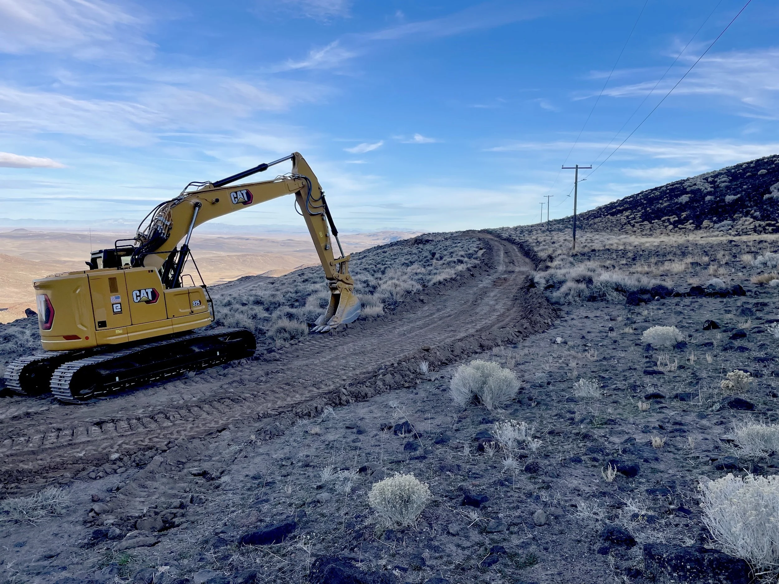 Excavator on a dirt road along a sagebrush hillside in Northern Nevada