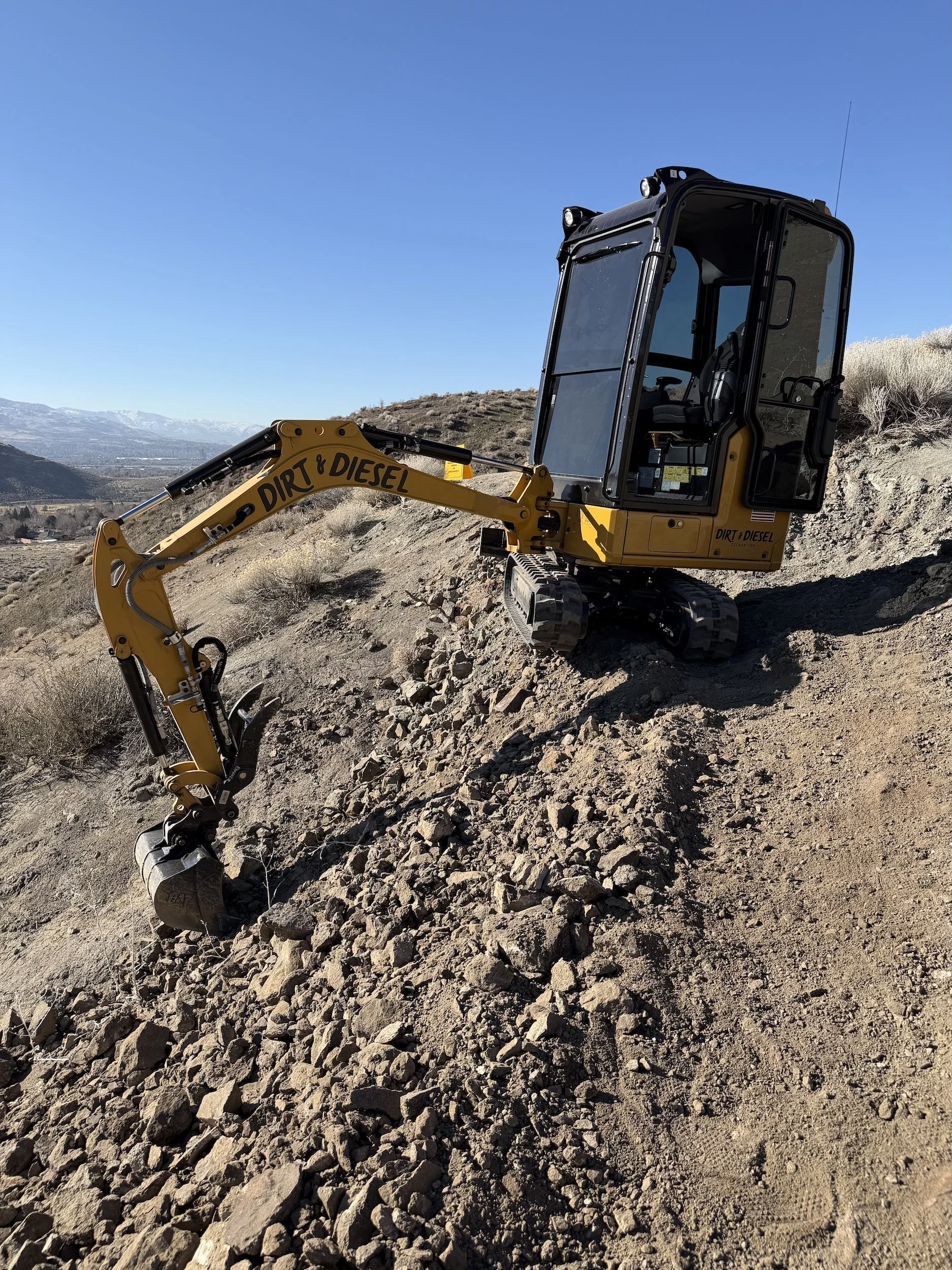  Compact Caterpillar excavator building trail on a steep, rocky decomposed granite slope in the Reno foothills. 