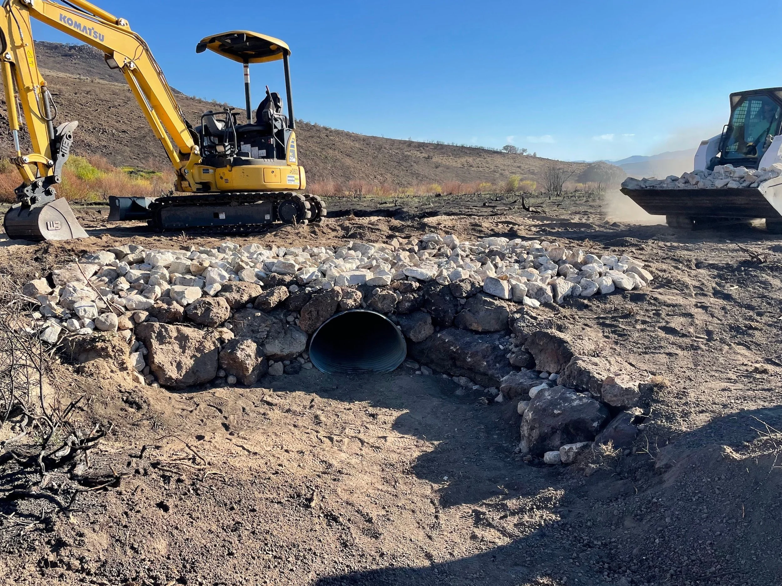 Excavator beside an installed culvert in a rock-lined drainage