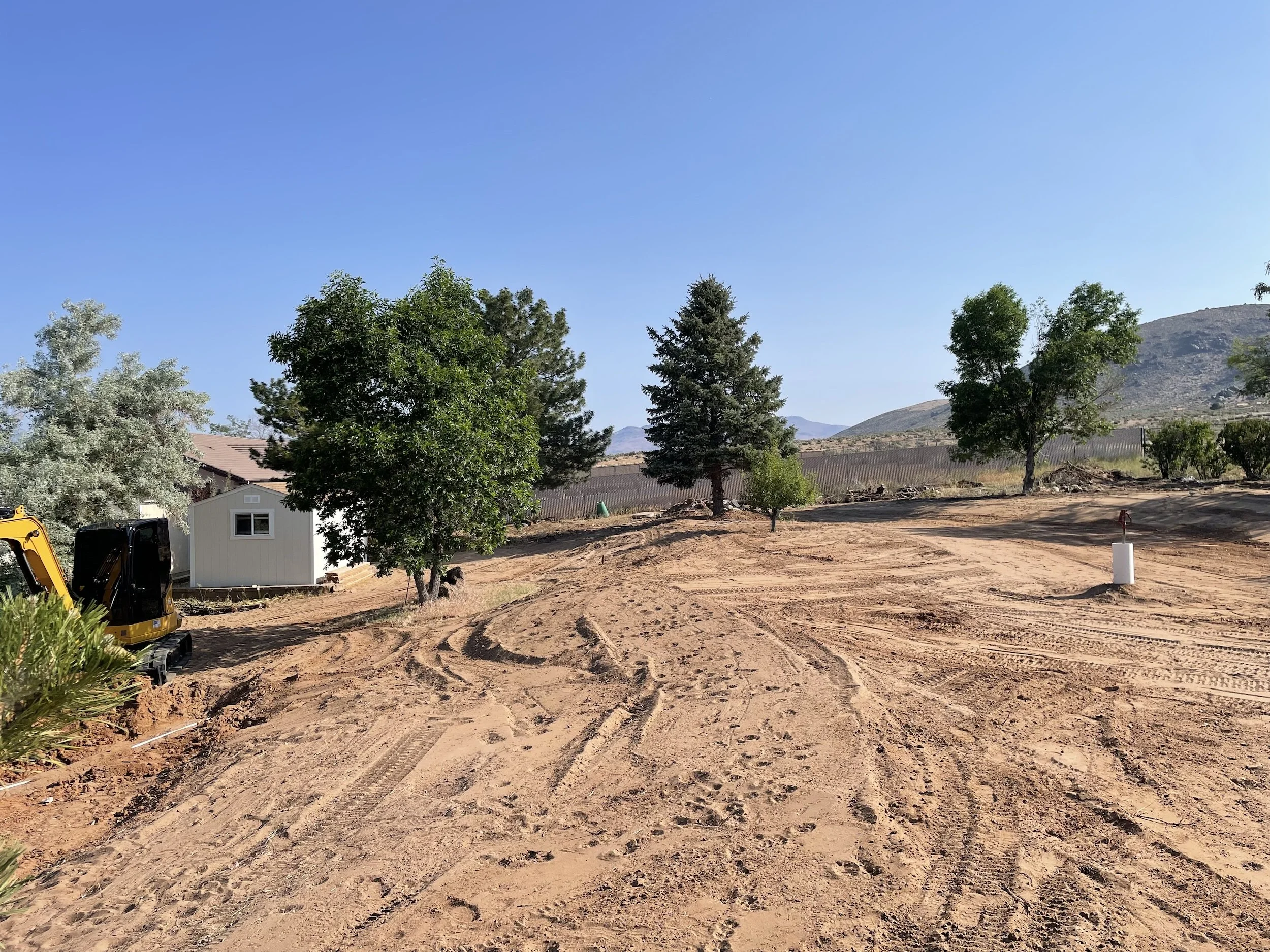 Graded homesite with tire tracks and trees, ready for construction