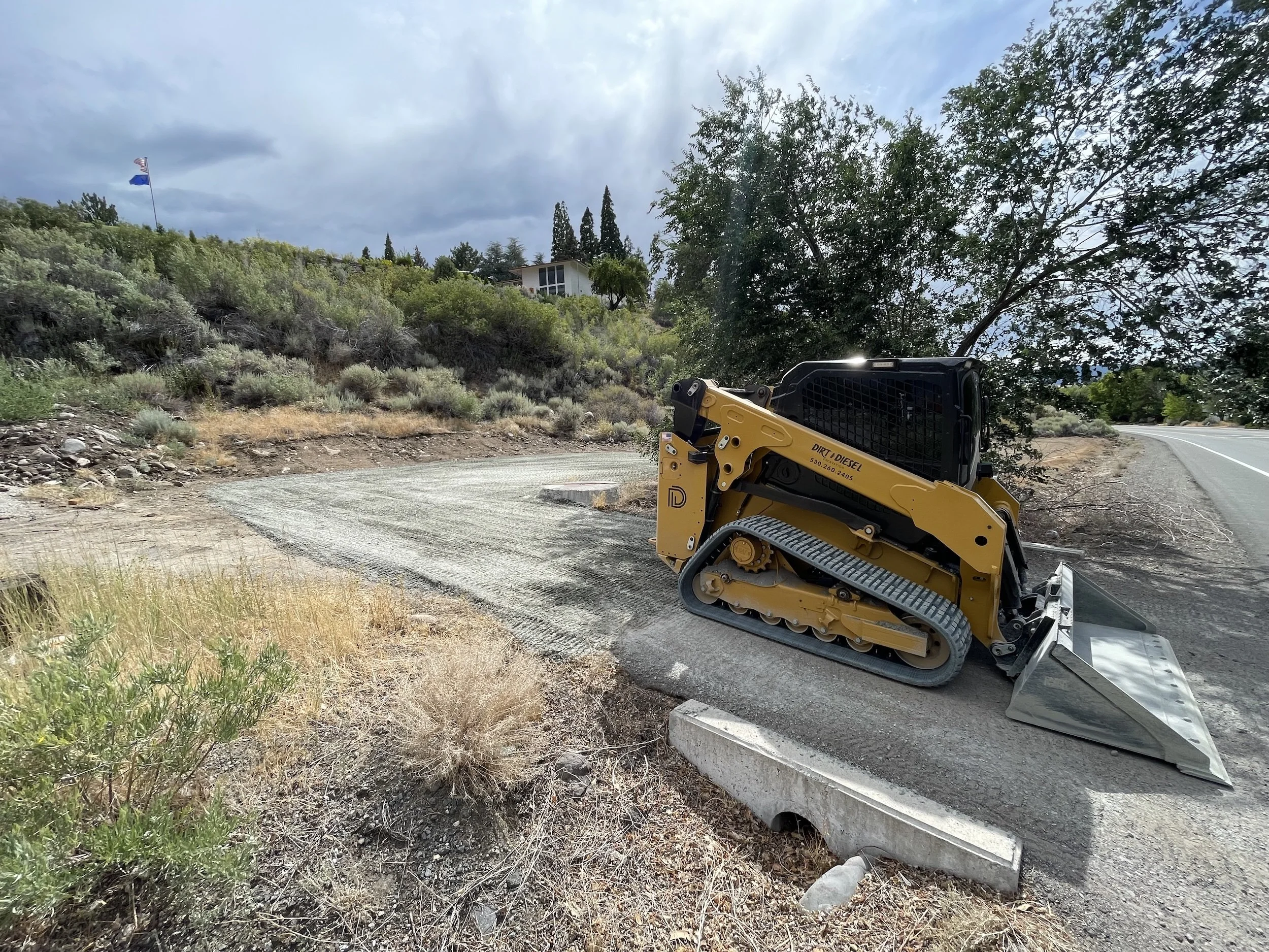 Track loader parked on a gravel road lined with trees