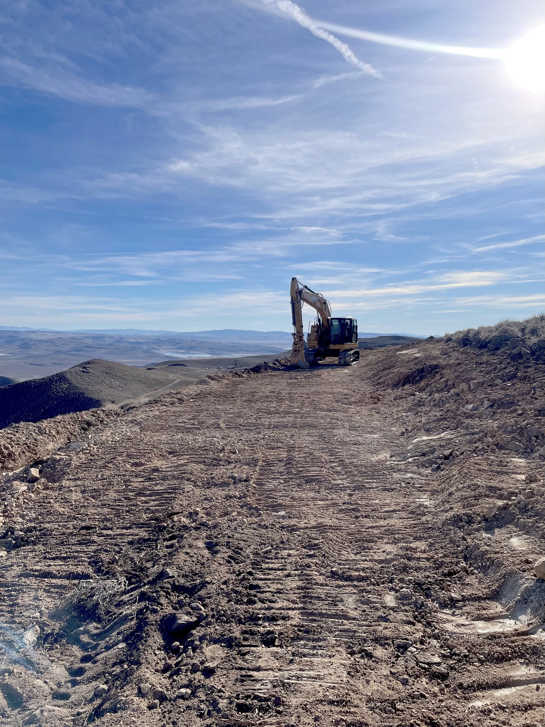 Excavator grading a large dirt pad on a hilltop