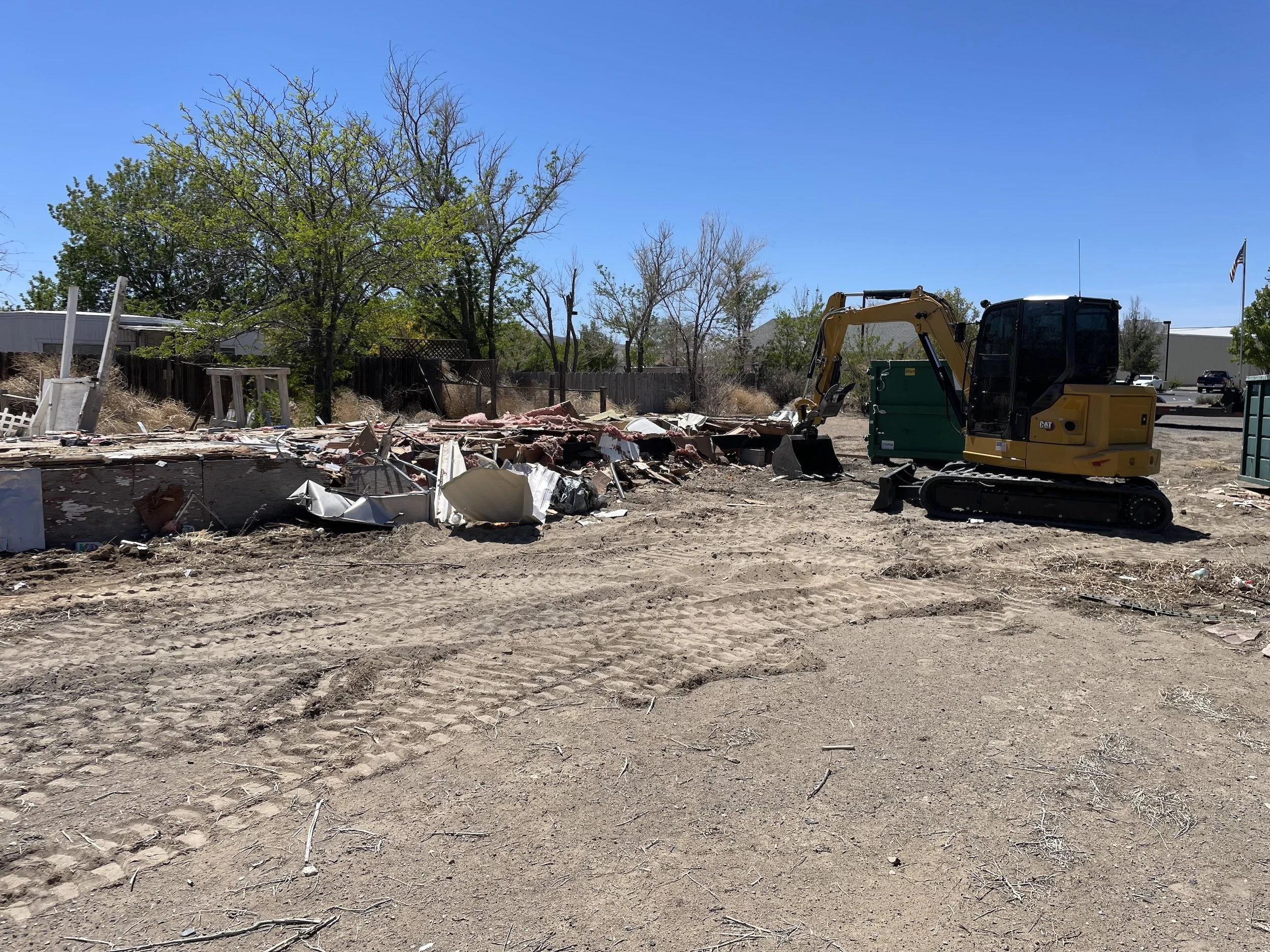 Cleared lot scattered with demolition debris and an excavator at the edge